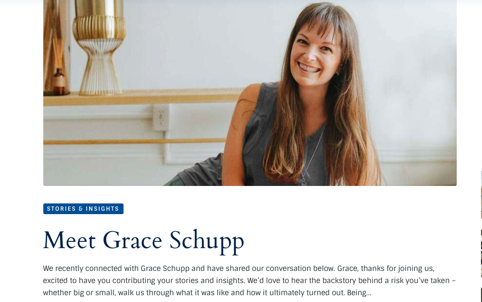 A woman with long brown hair wearing a sleeveless gray top, smiling in a bright room with a white wall and a decorative lamp in the background.