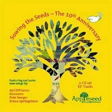 Cover of a music album titled 'Soaring the Seeds - The 10th Anniversary' with a yellow background includes Lizzie West. It mentions featuring exclusive new songs by artists Anil D'Silva, Danavann, Pete Seeger, and Bruce Springsteen.