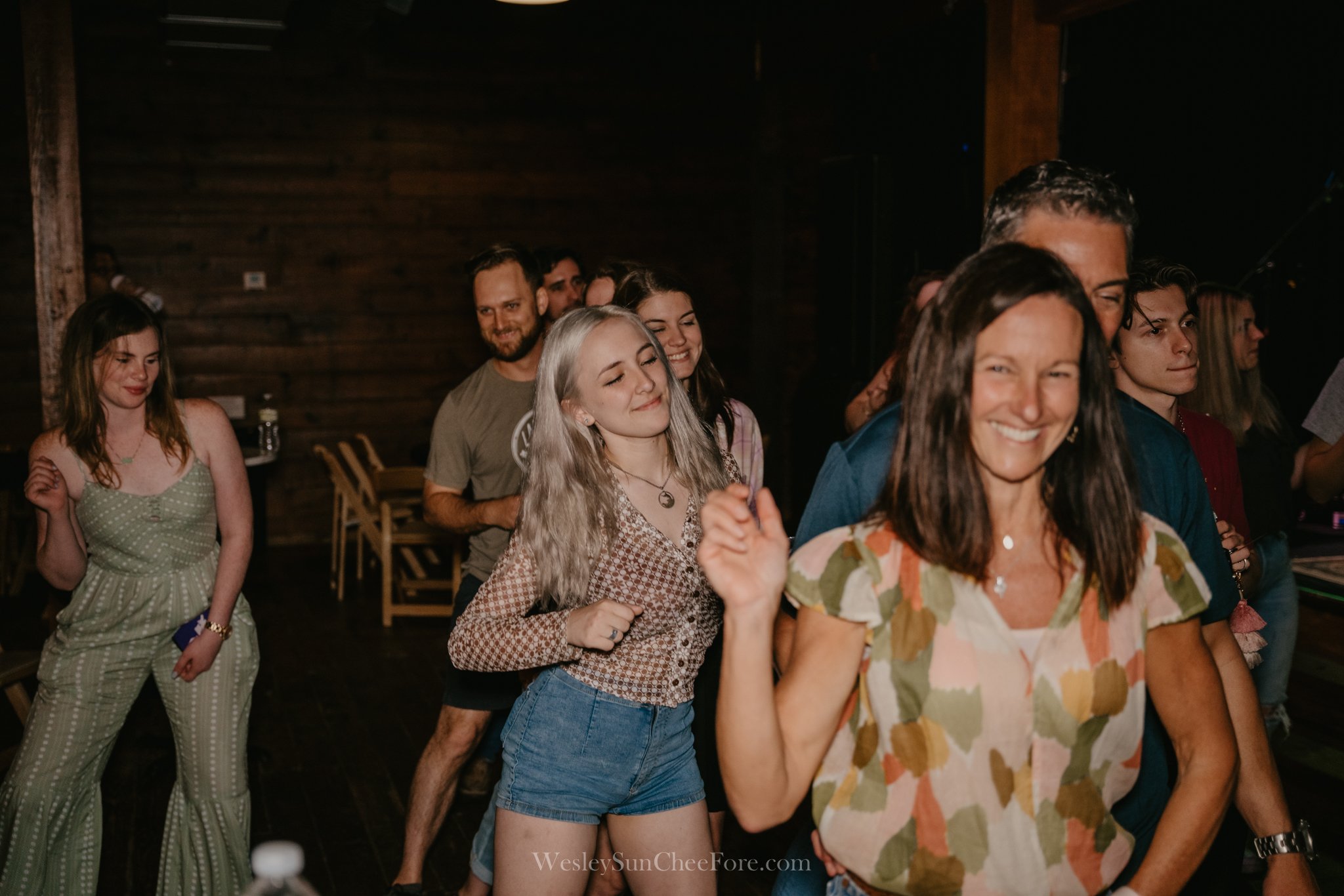 People dancing and smiling at a social gathering or party in a dimly lit wooden venue.