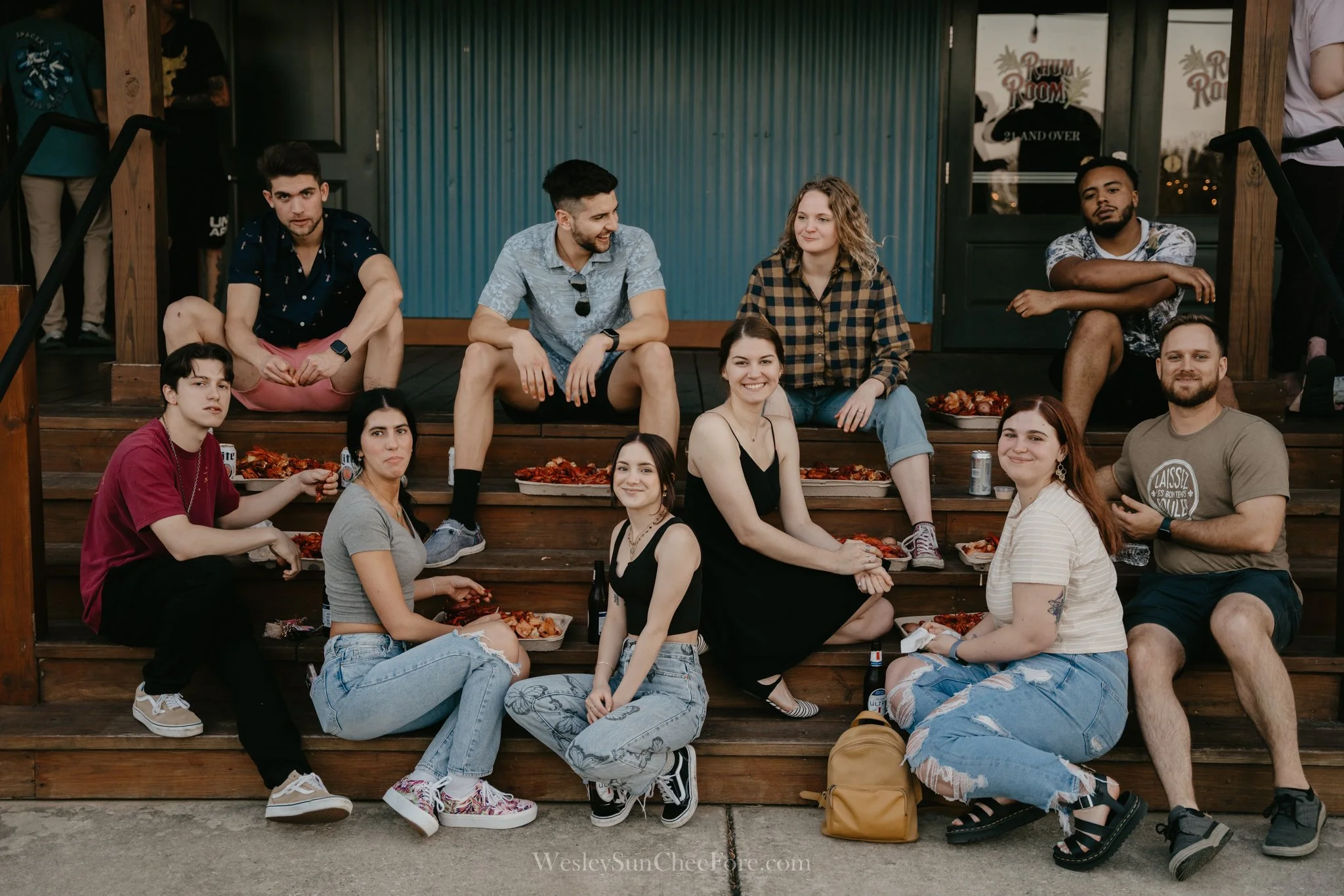 Group of ten young adults sitting on wooden steps outside, eating pizza, and socializing.