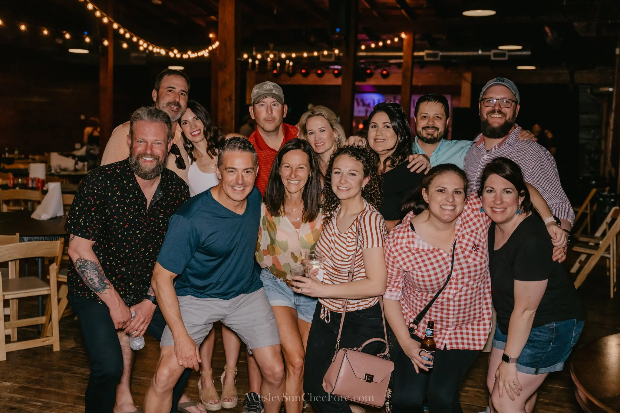 Group of friends at a social event in a rustic indoor venue with string lights, smiling and posing together.