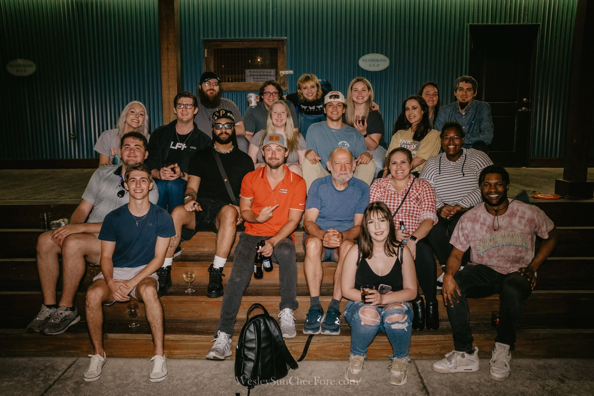 A large group of people smiling and posing on wooden steps indoors, at a party or social gathering.
