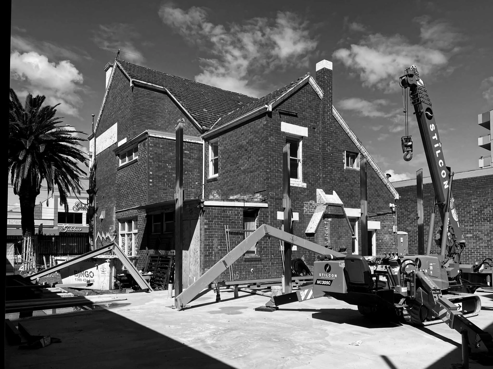 Construction site with a brick building in progress, a crane labeled 'STILCON', and construction materials scattered on the ground.