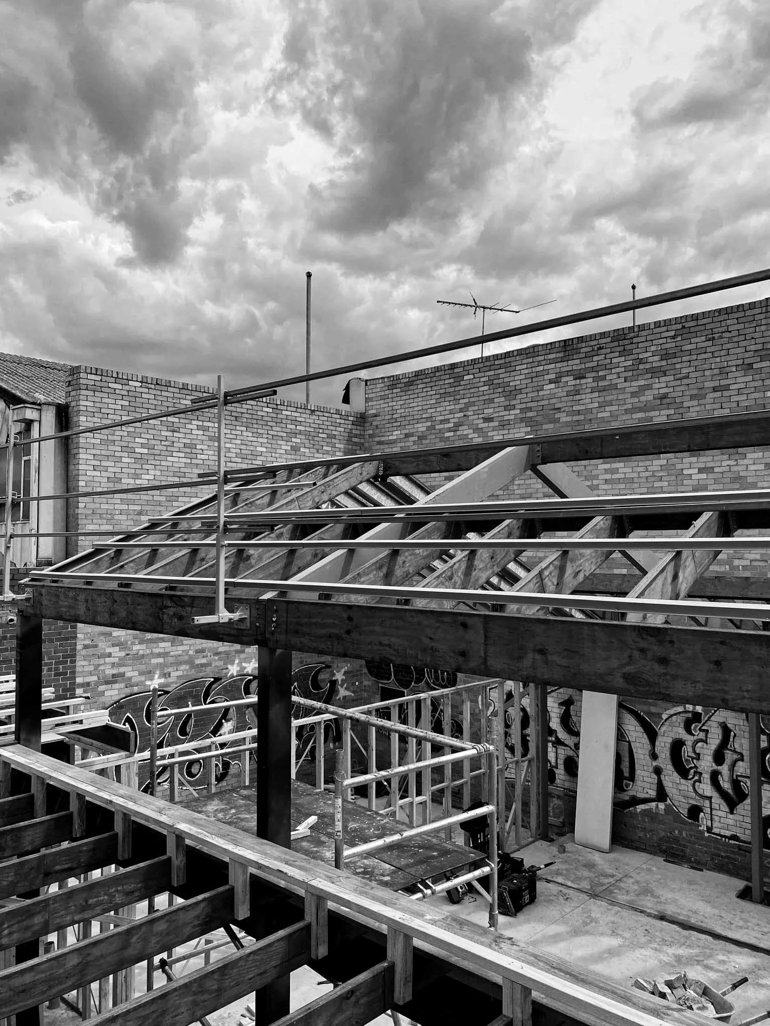 Construction site on a rooftop with scaffolding, brick walls, and graffiti, under a cloudy sky.