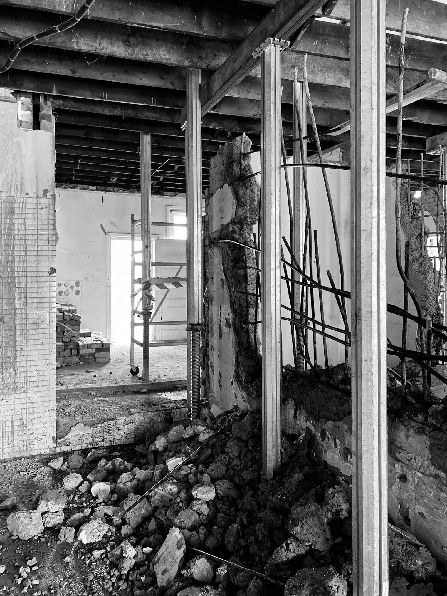 Interior view of a building under construction with exposed concrete, steel rebar, scaffolding, and debris on the floor.
