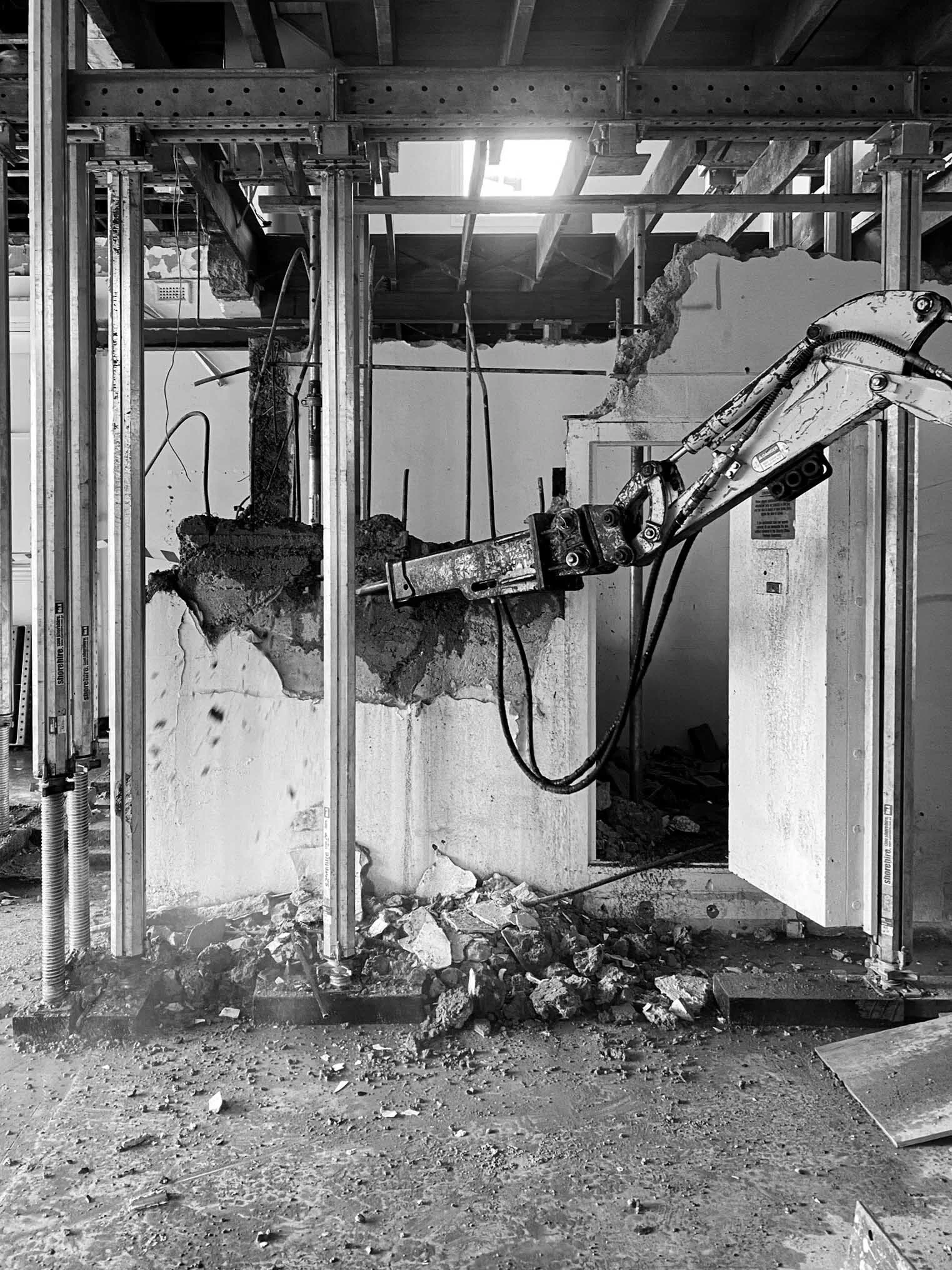 Construction site featuring a hydraulic demolition excavator breaking through a concrete wall with debris on the ground.