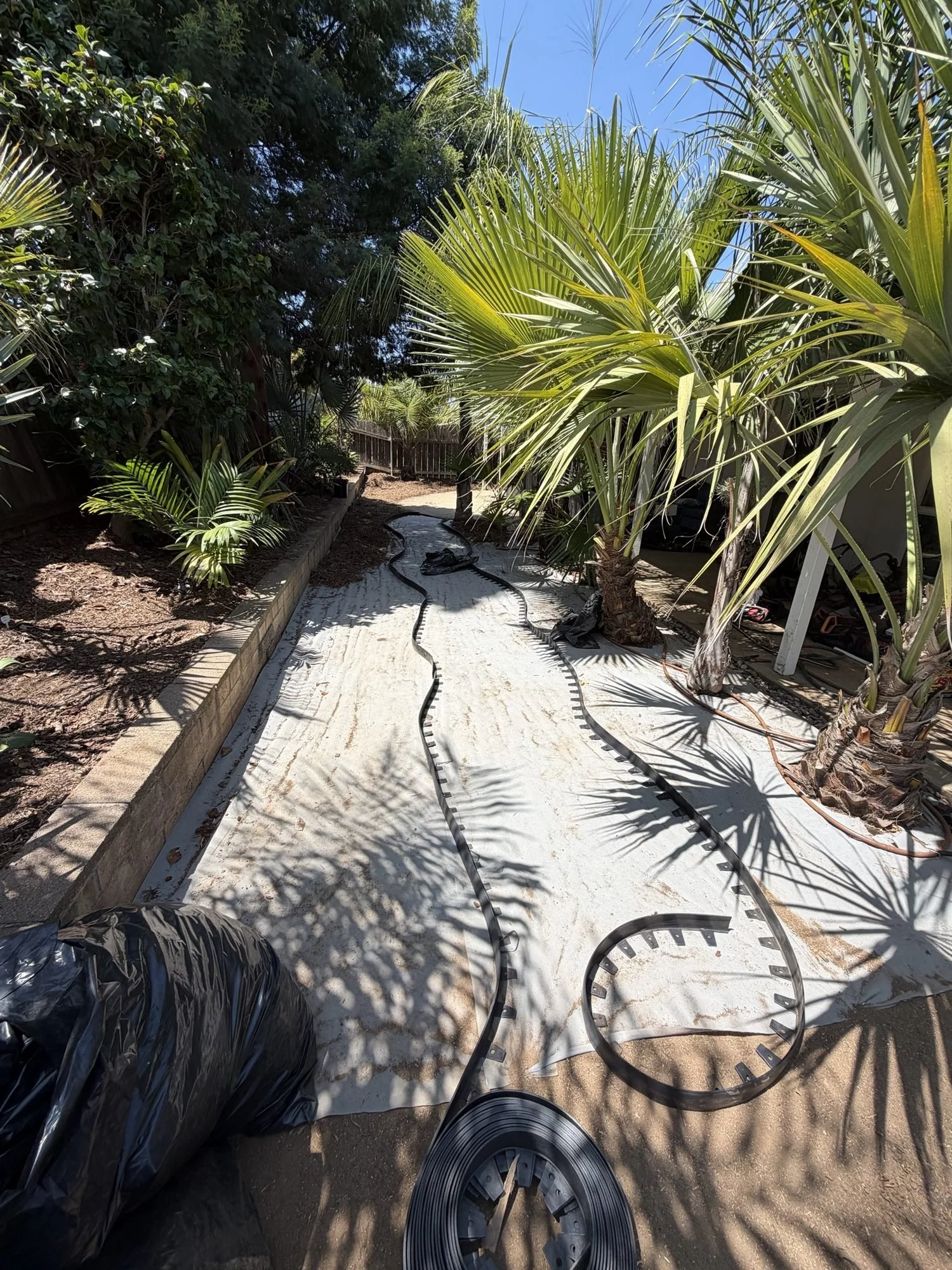 Landscape fabric and staked black edging laid for curving decomposed granite paths during installation in San Diego