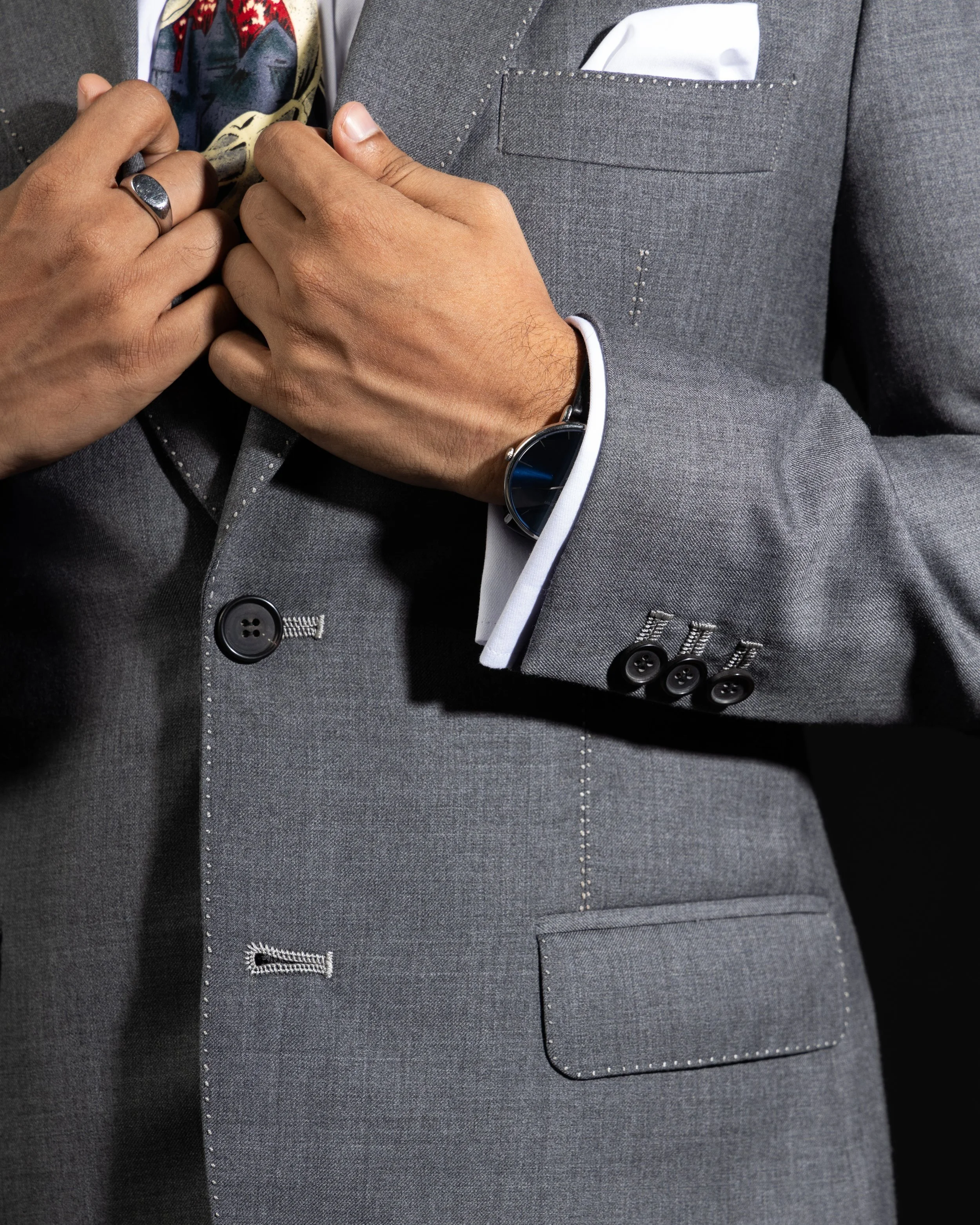 Close up of the front of a grey suit jacket, focusing on the hand finishes of the pockets and button holes