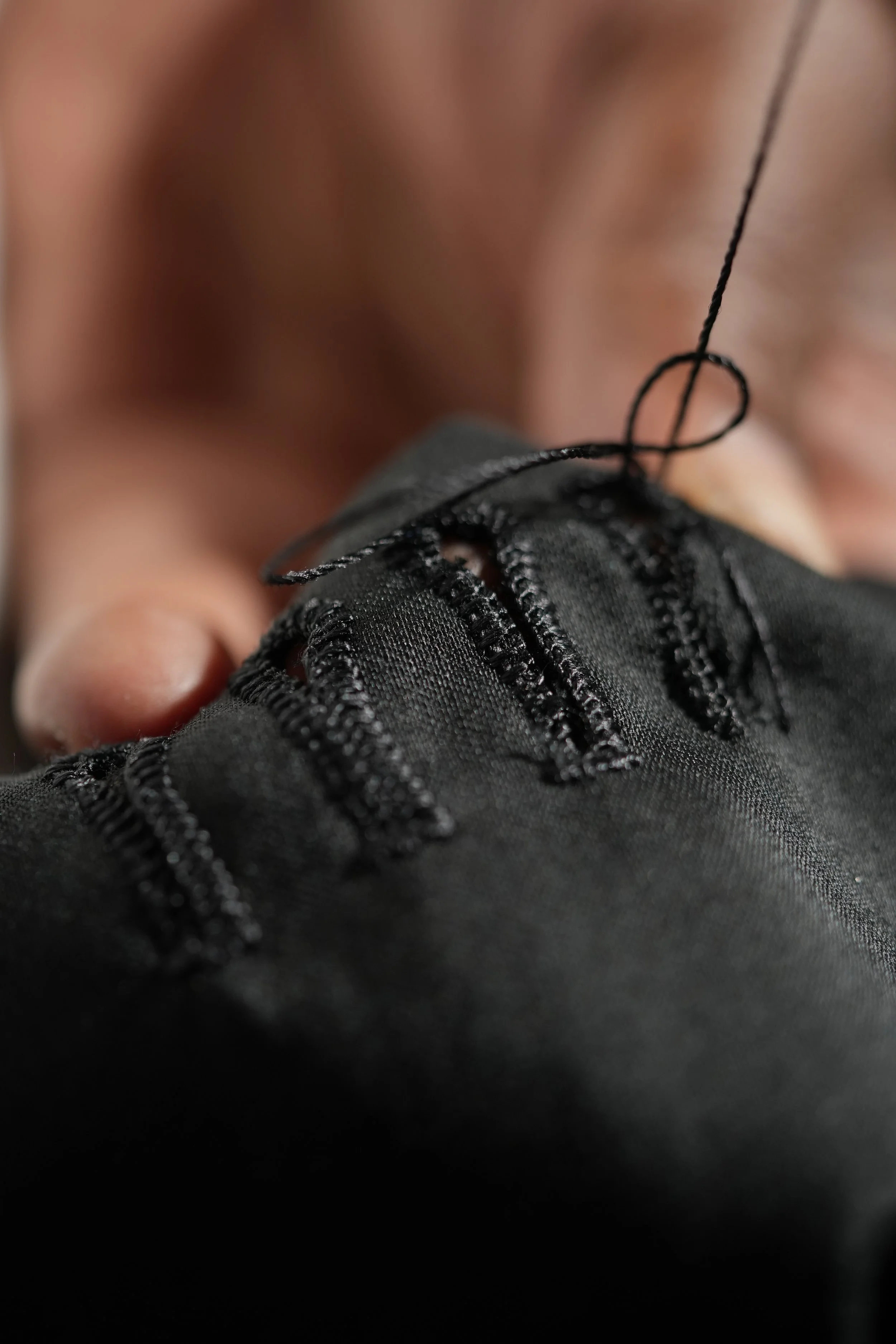 Close up of hand sewing the button holes of a suit jacket