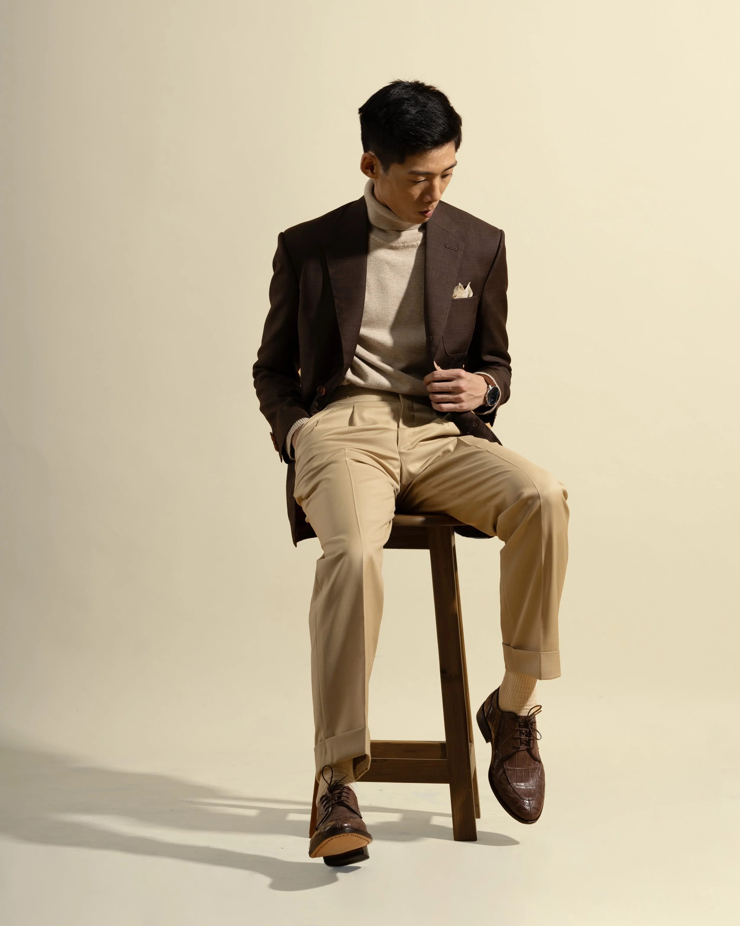 A model sitting and wearing a Sein Shwe bespoke cacao brown blazer and yellow cream trousers