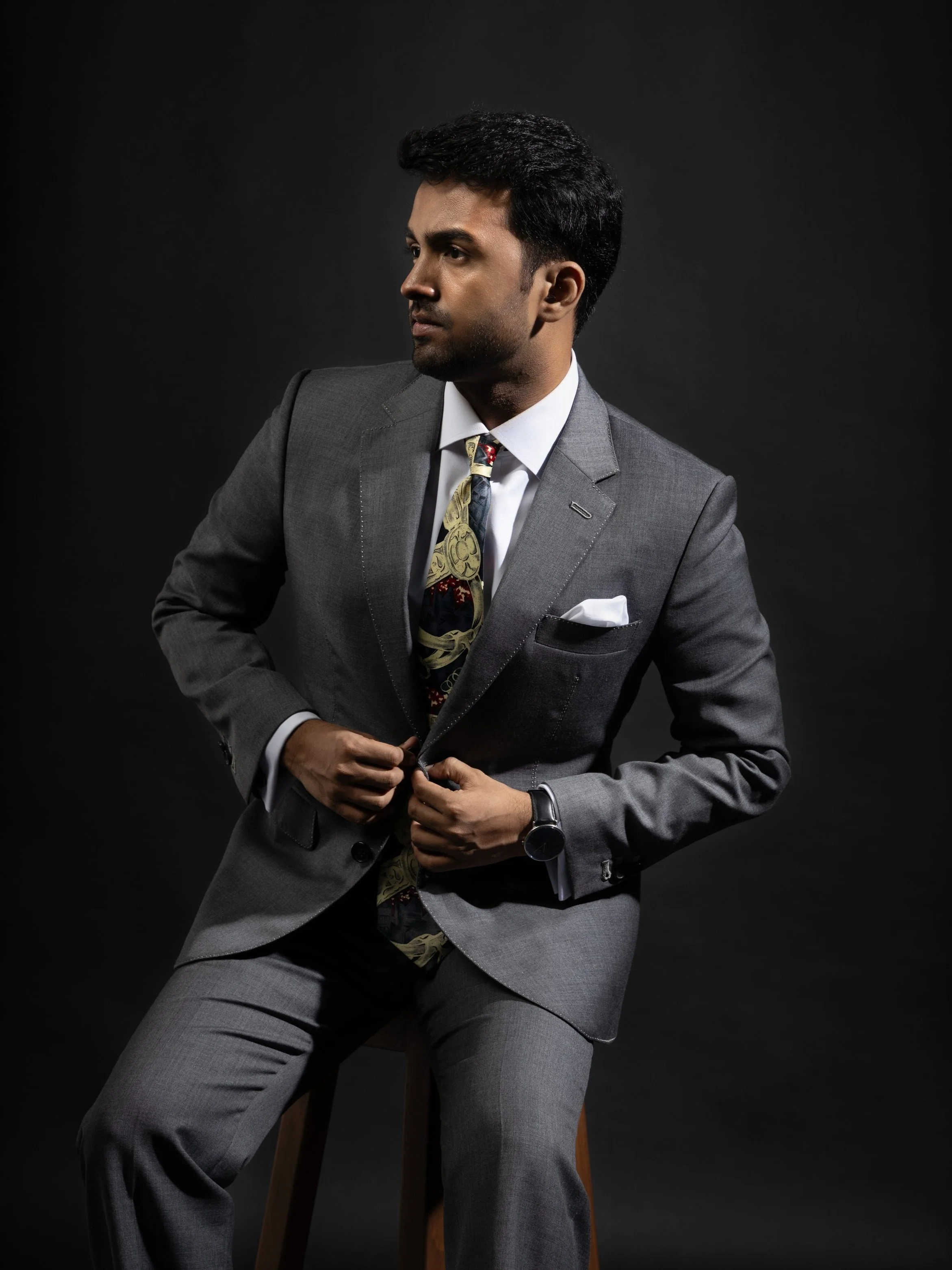 A model seated wearing a 2-piece grey bespoke Sein Shwe suit