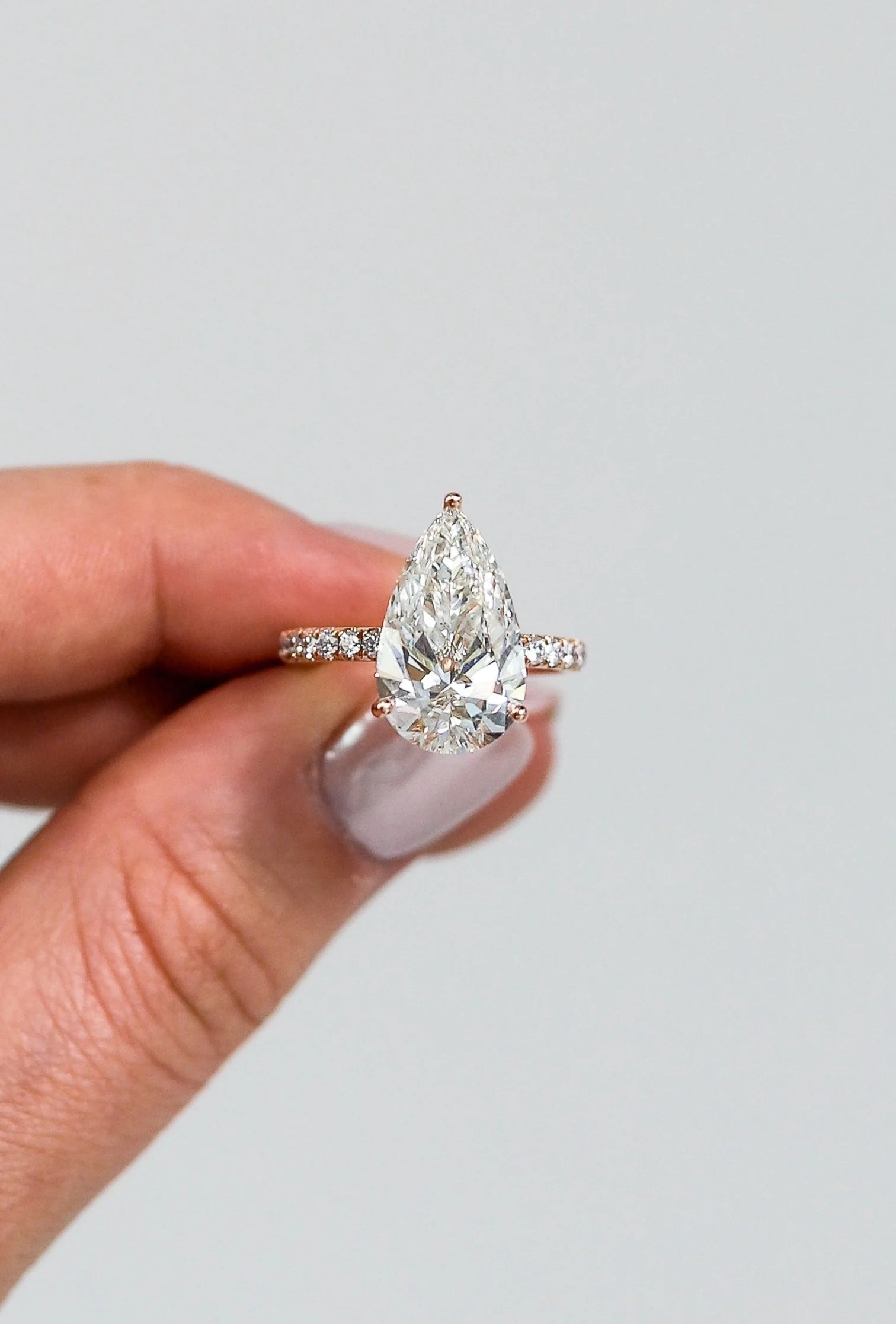 A hand holding a large pear-shaped diamond engagement ring with a diamond-studded band.
