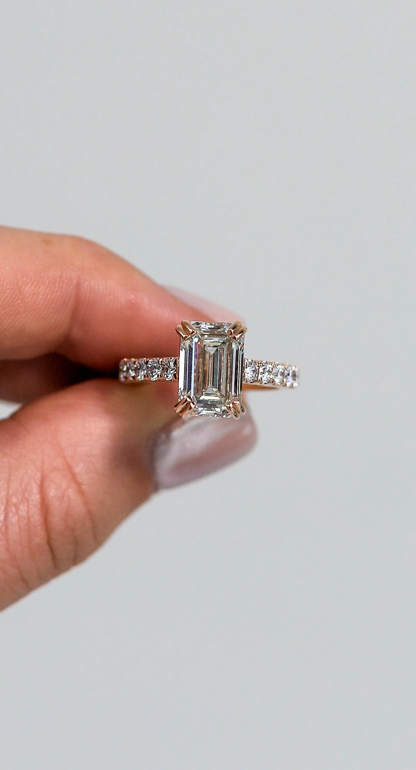 Close-up of a hand holding a diamond engagement ring with a rectangular emerald-cut diamond and smaller diamonds along the band.