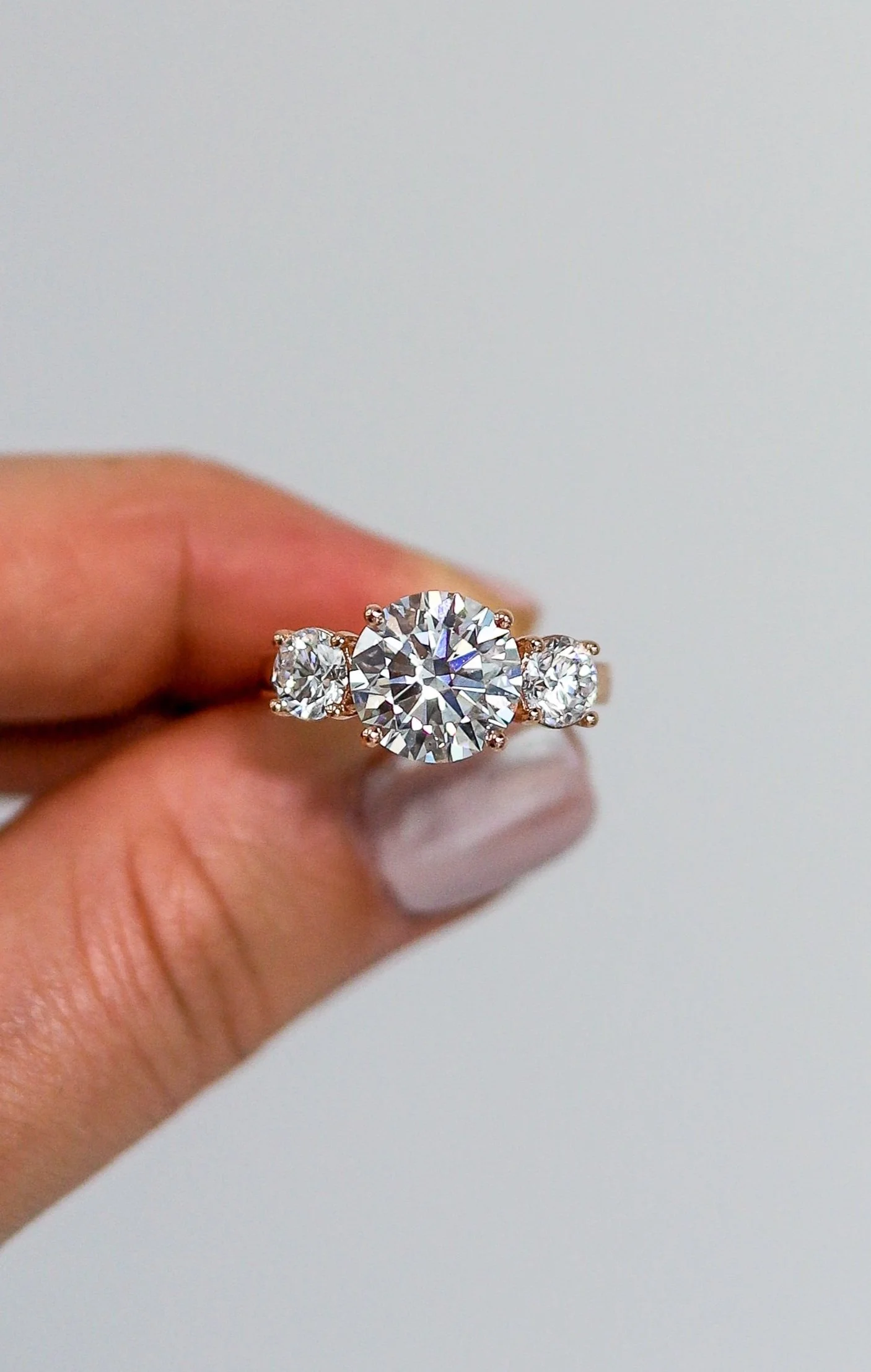 Close-up of a hand holding a silver ring with three large diamonds, two smaller diamonds on each side, against a plain light background.