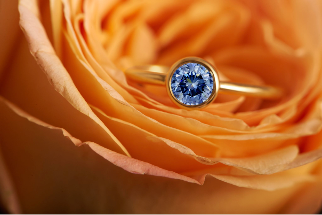 Ein blauer EverDear-Erinnerungsdiamant in einem Goldring, gebettet in die Blütenblätter einer Rose, als Symbol für einen geliebten Menschen, der nahe bleibt.