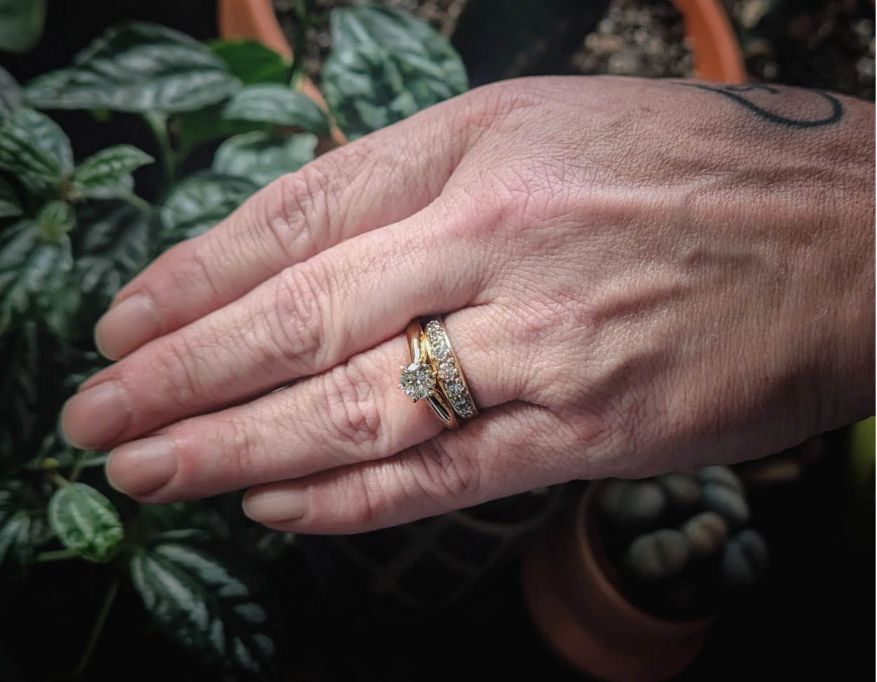 Eine Hand mit einem Goldring, besetzt mit einem EverDear-Erinnerungsdiamanten, vor Zimmerpflanzen in einer warmen Wohnatmosphäre.