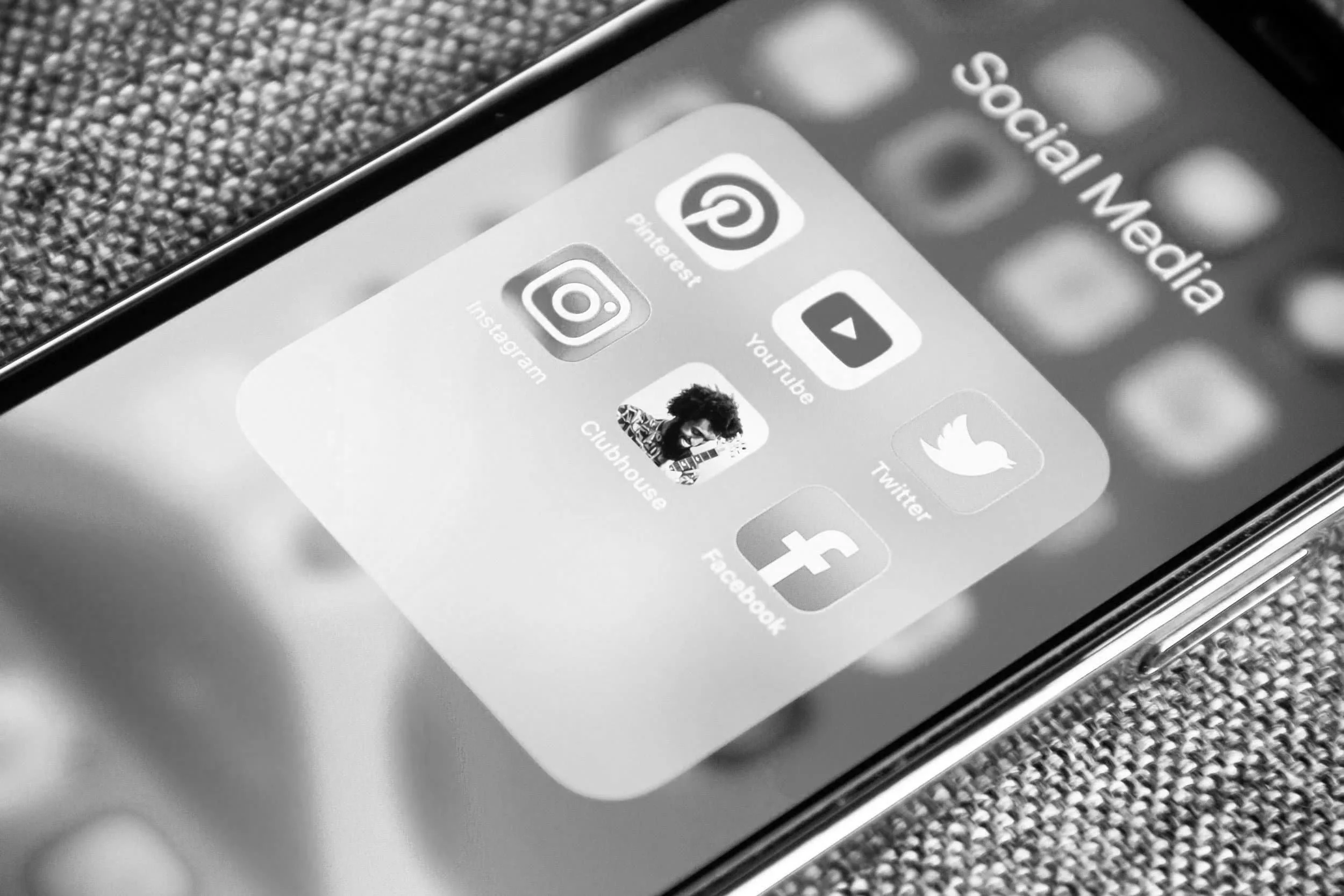 Black-and-white close-up of a smartphone displaying social media app icons for Instagram, Pinterest, YouTube, Twitter, and Facebook.