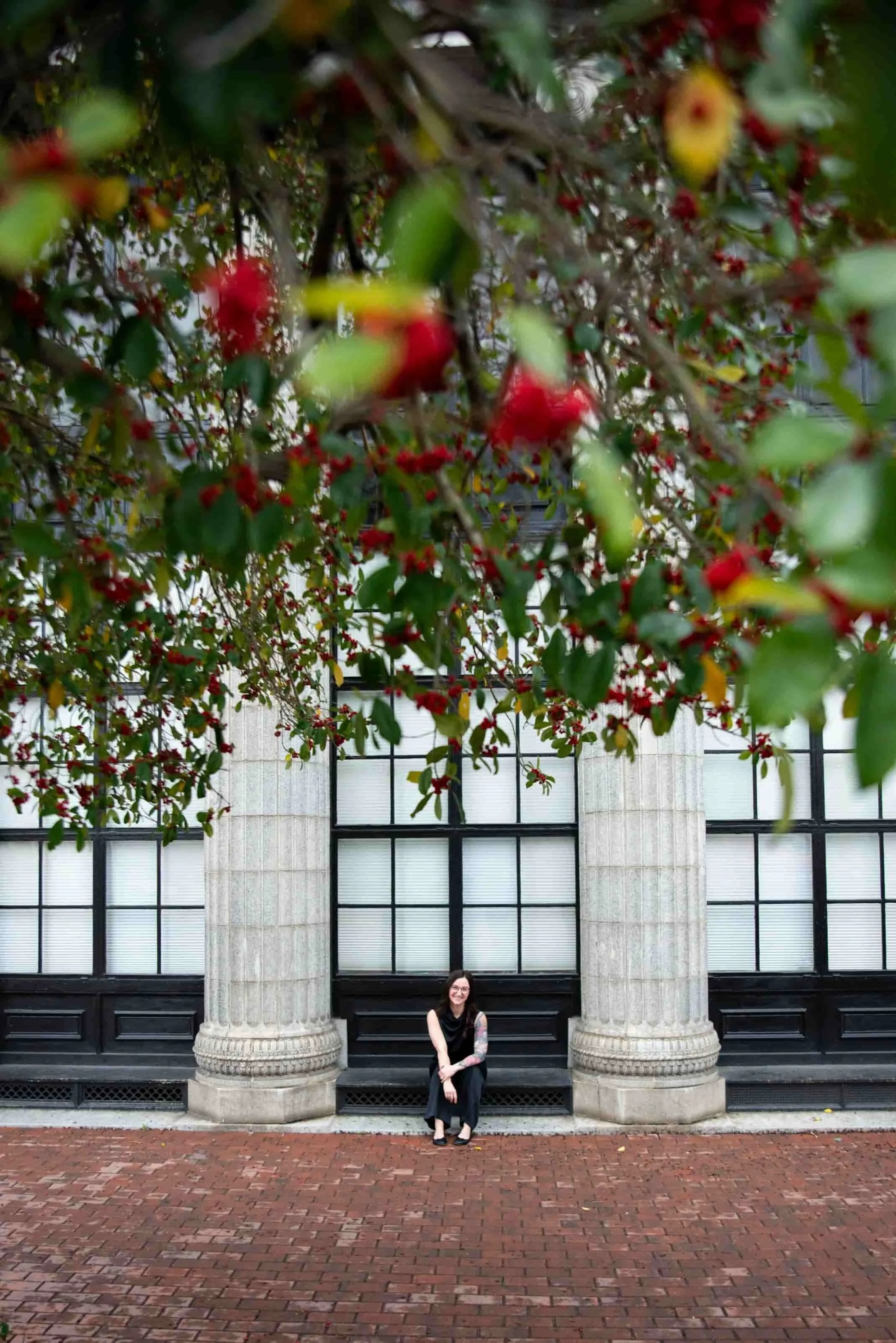 Woman in black sitting between large stone planters covered with red berries in front of a historic building