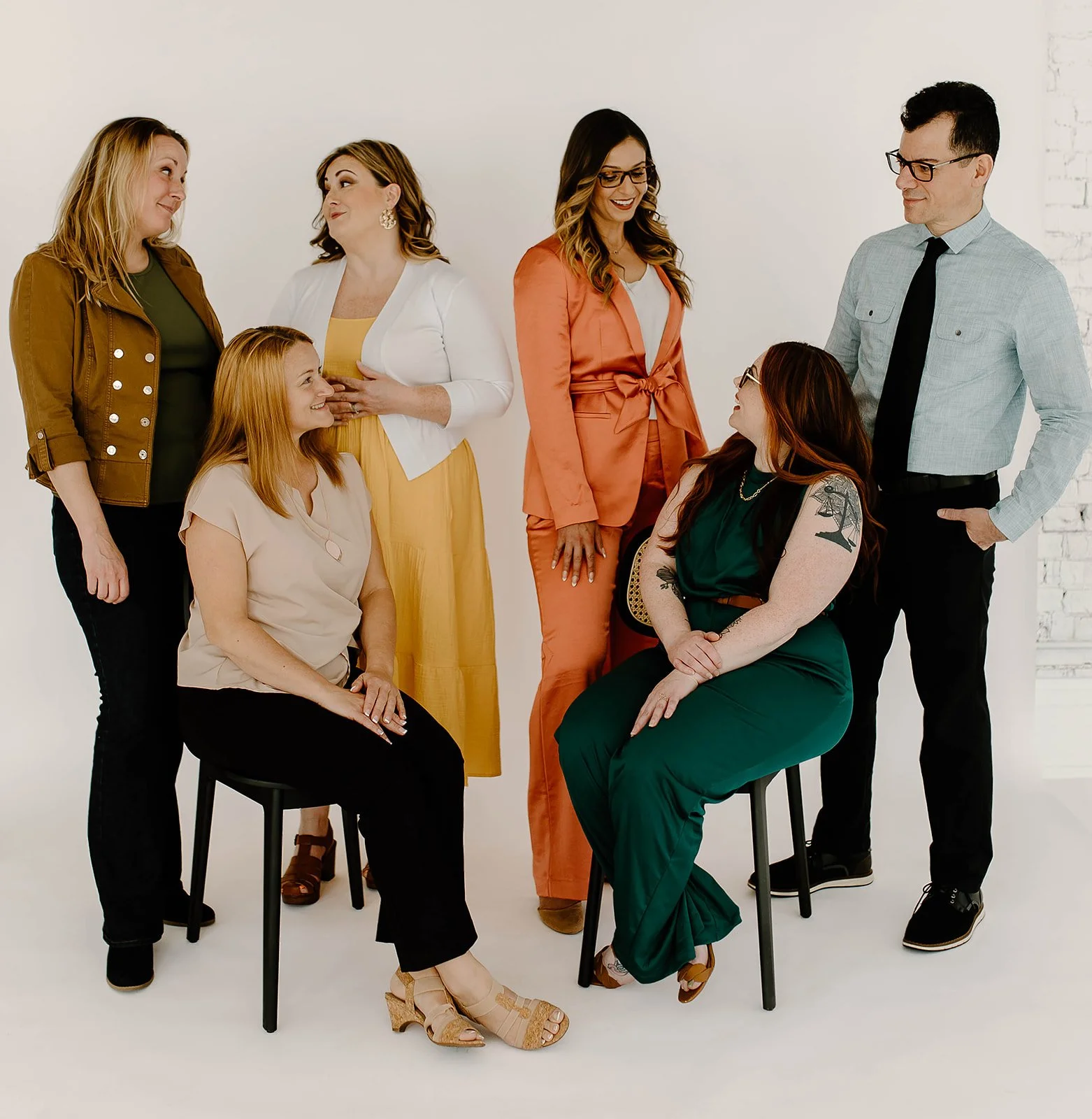 Group of six people smiling, standing and sitting together in business casual attire against a white background.