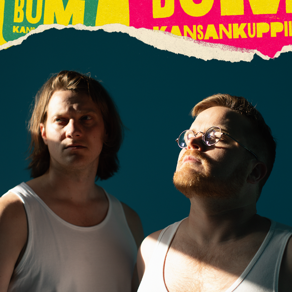 Kaksi miestä seisoo varjossa, toinen katsoo ylös ja toinen katsoo sivulle. Heillä on valkoiset tanktopit ja taustalla värikäs koristeellinen teippi, jossa on tekstiä.
