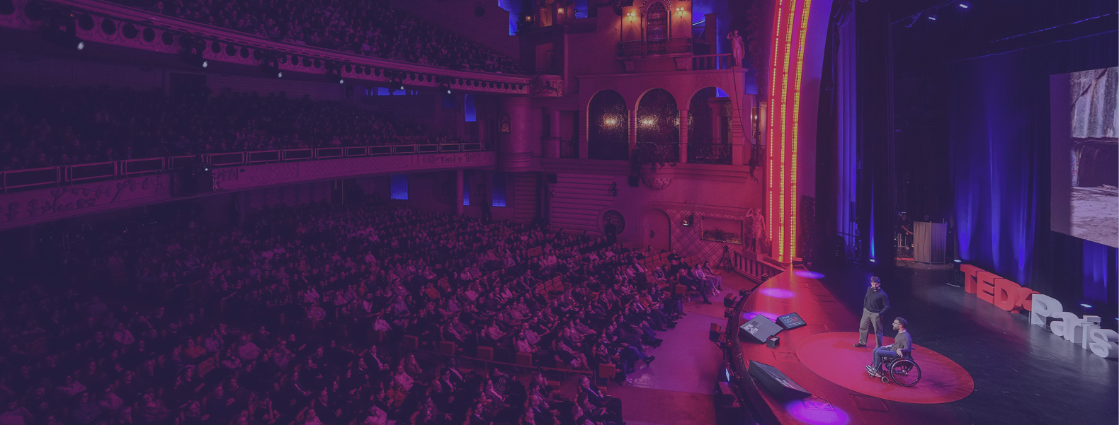 Deux intervenants sur la scène d’un événement TEDx devant un large public dans un théâtre rempli