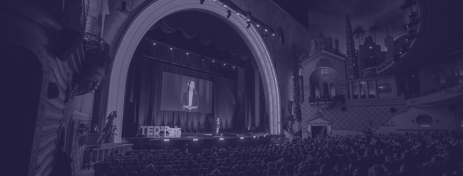 Conférencier sur scène lors d’un événement TEDx devant une grande audience dans un théâtre rempli.