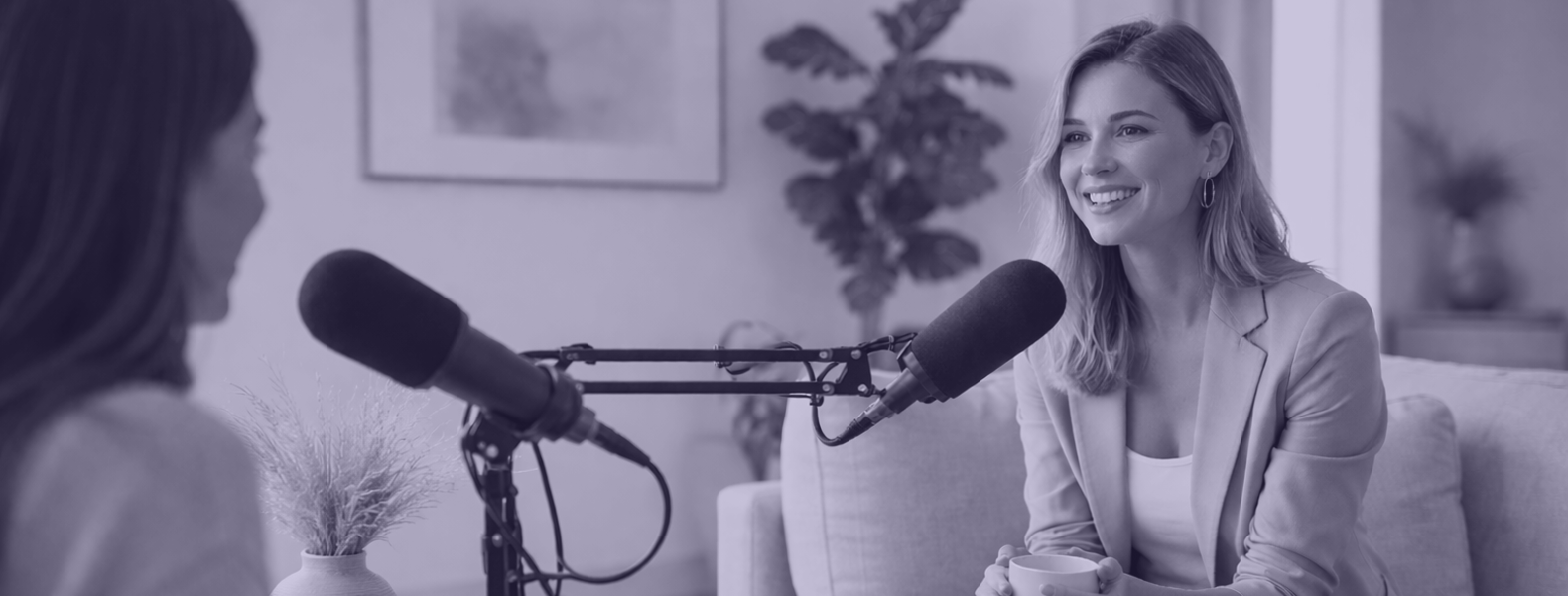 Femme interviewée dans un podcast par une autre femme dans un salon moderne et minimaliste avec microphones et canapé beige.