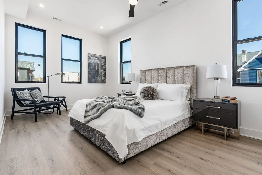 Modern bedroom with a bed, nightstands, lamps, a chair, and large windows