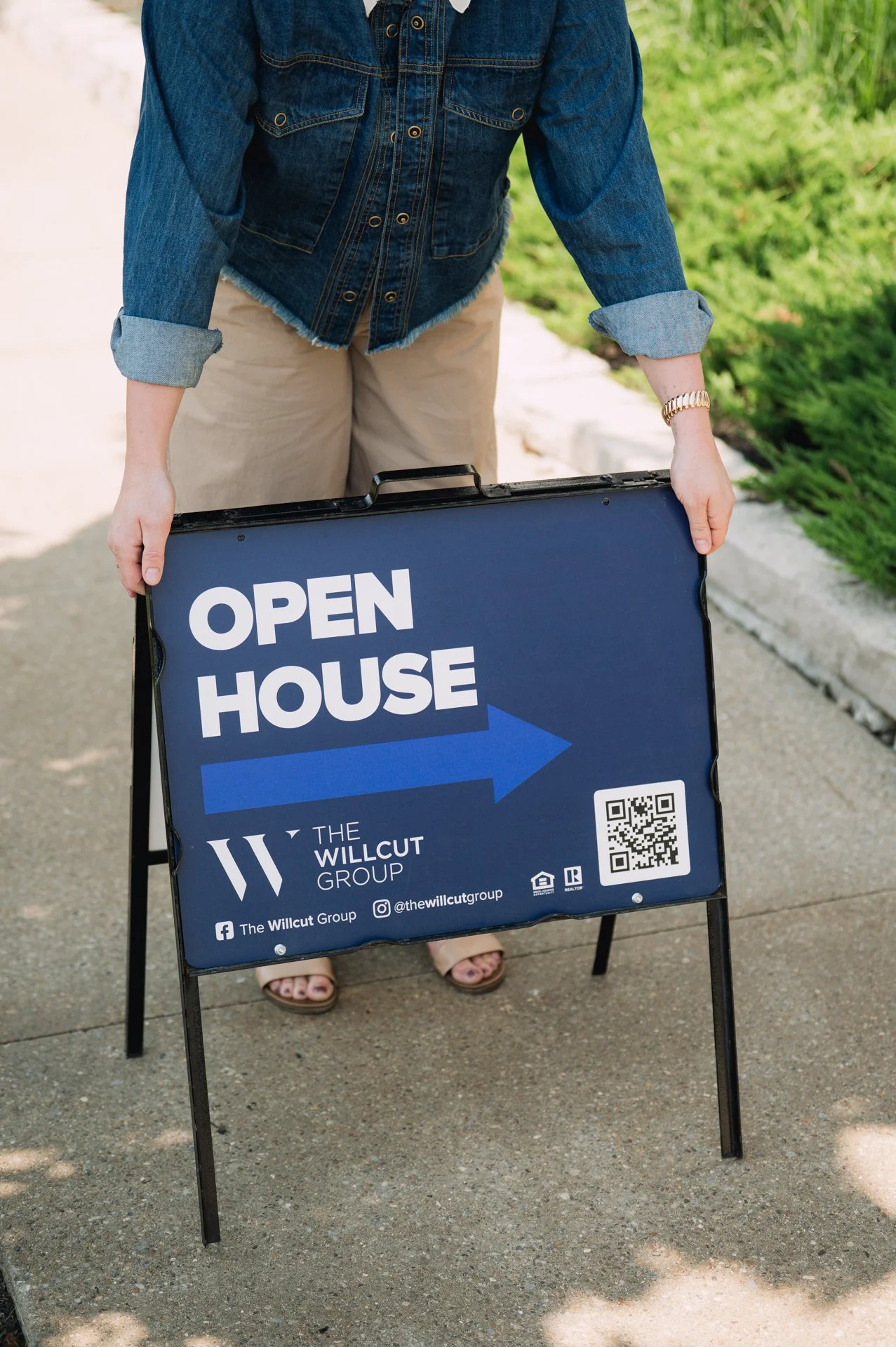 Signboard for open house event held by The Willcut Group, with an arrow pointing to the right, placed outdoors on a sidewalk.