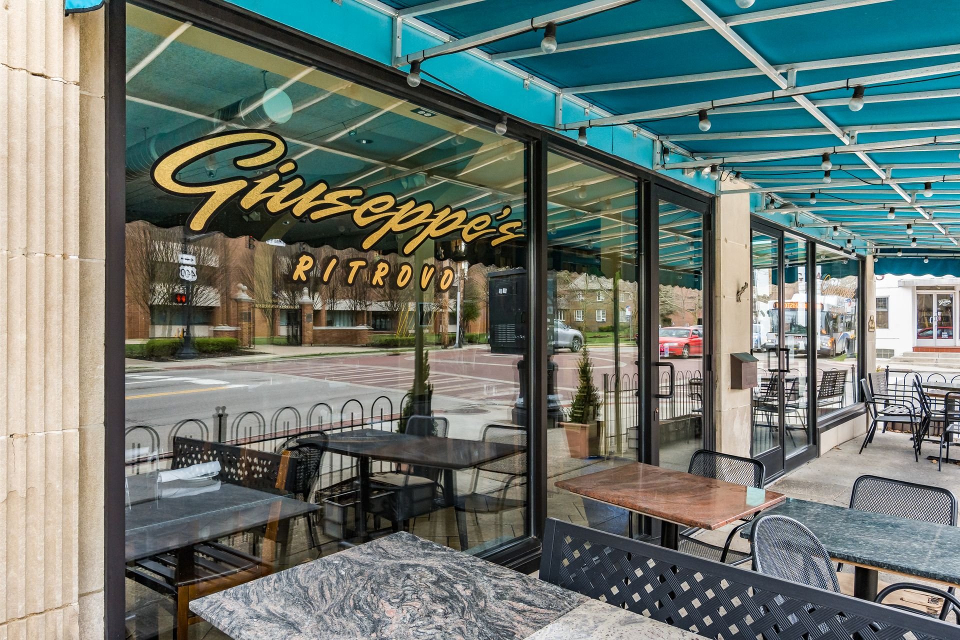 Outdoor seating area of Giuseppe's Ritrovo restaurant with tables and chairs under a blue awning.