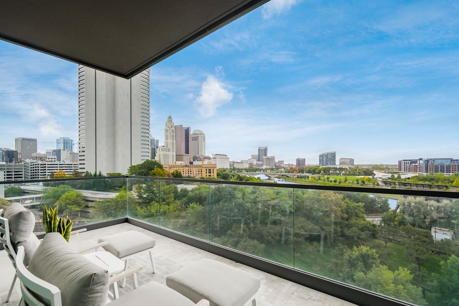 Skyline view from a balcony overlooking a city with modern high-rise buildings, green park area, and blue sky.