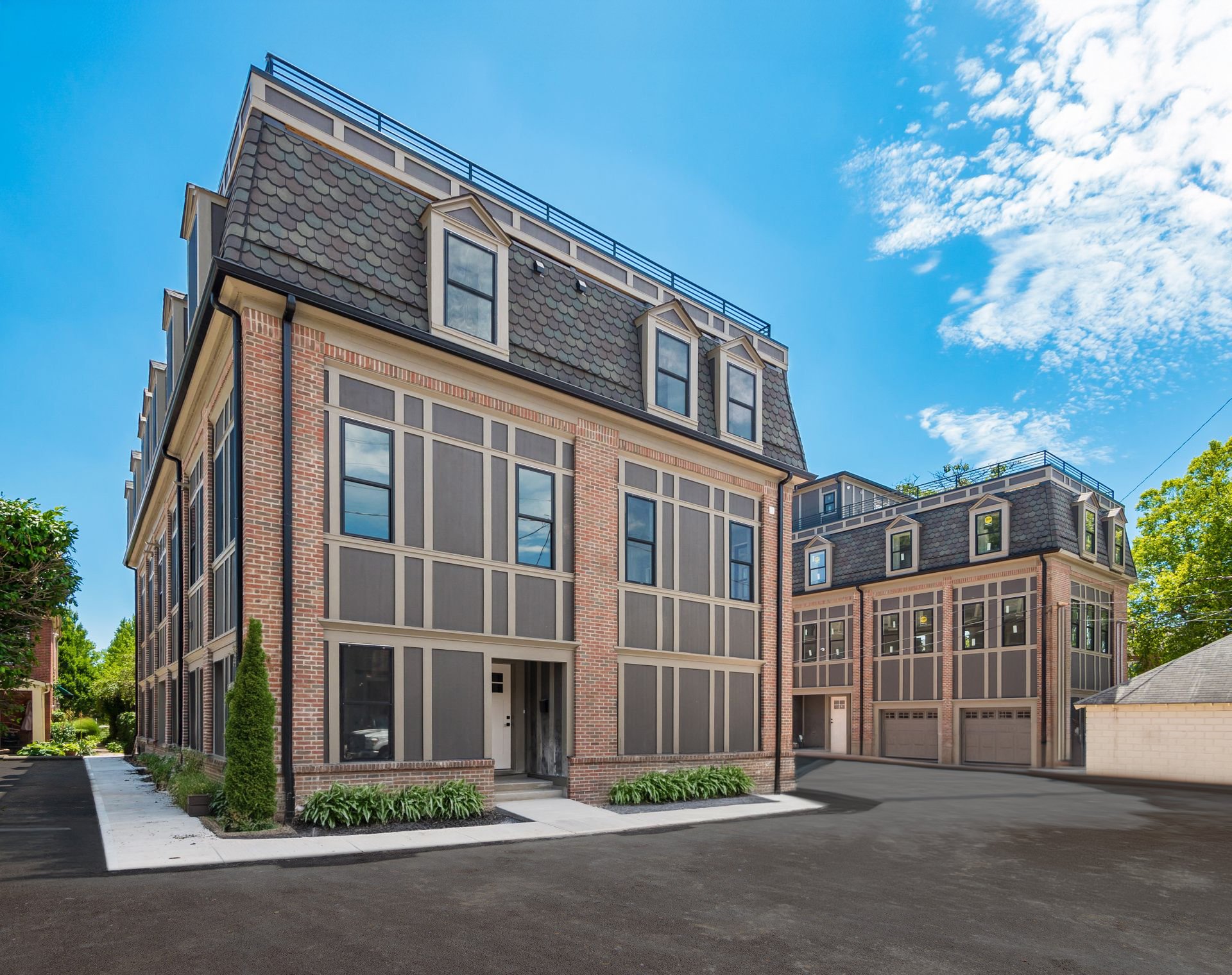 Modern multi-story townhouses with brick and panel exterior, large windows, and rooftop terraces under a clear blue sky.
