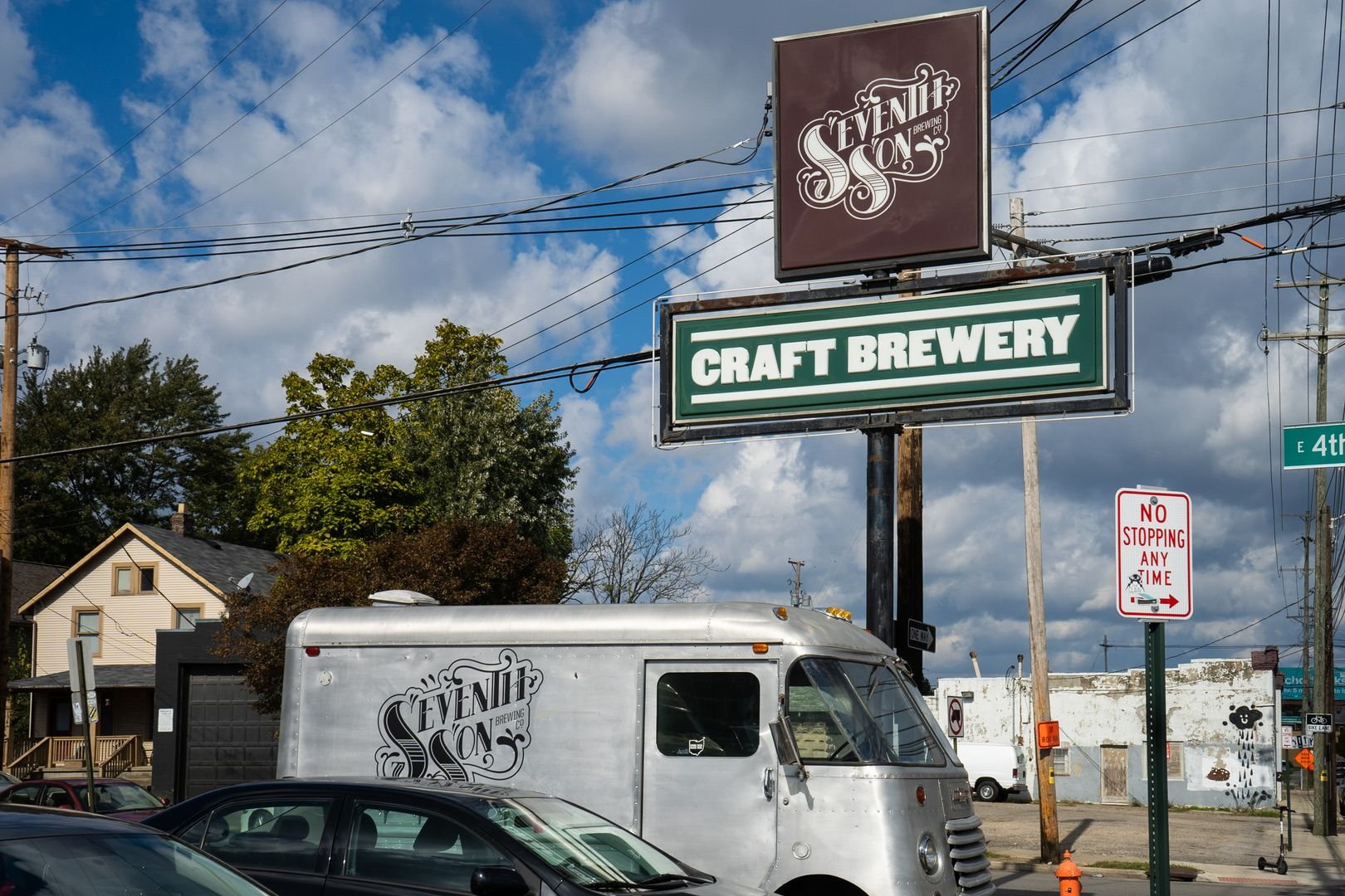 Craft brewery signage and branded vehicle in an urban setting with houses and street signs.