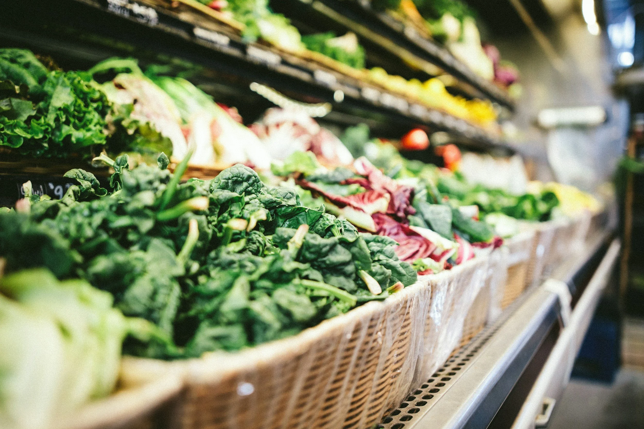 Fresh leafy greens and vegetables arranged in a basket display at a grocery store or market.