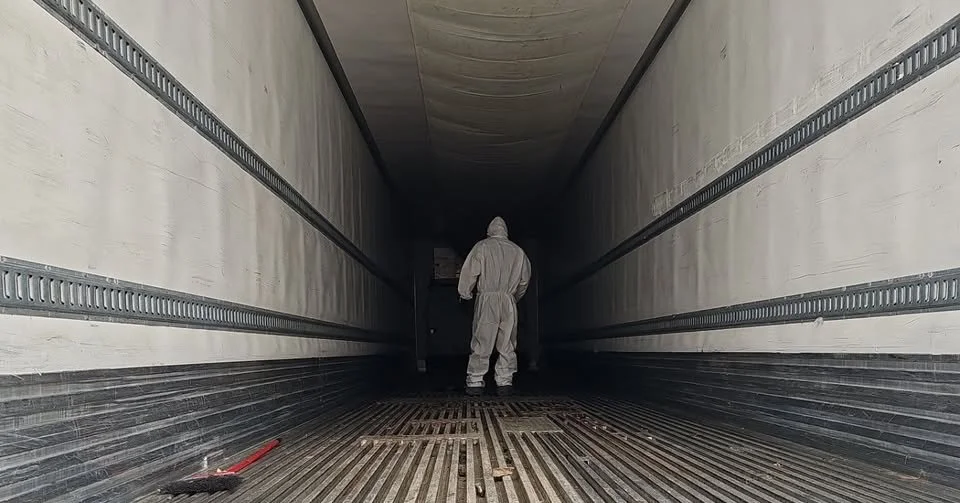 Trauma cleaner in protective suit walking inside a cargo truck or container.