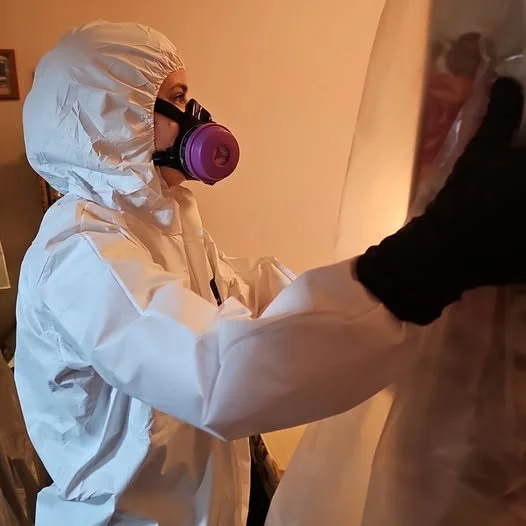 A trauma cleaer in full protective gear, including a protective suit, gloves, and a respirator mask.