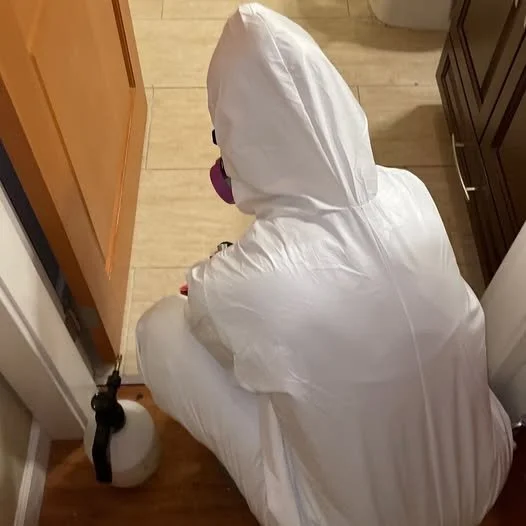 Biohazard cleaning technician in a white protective suit cleaning a bathroom floor.