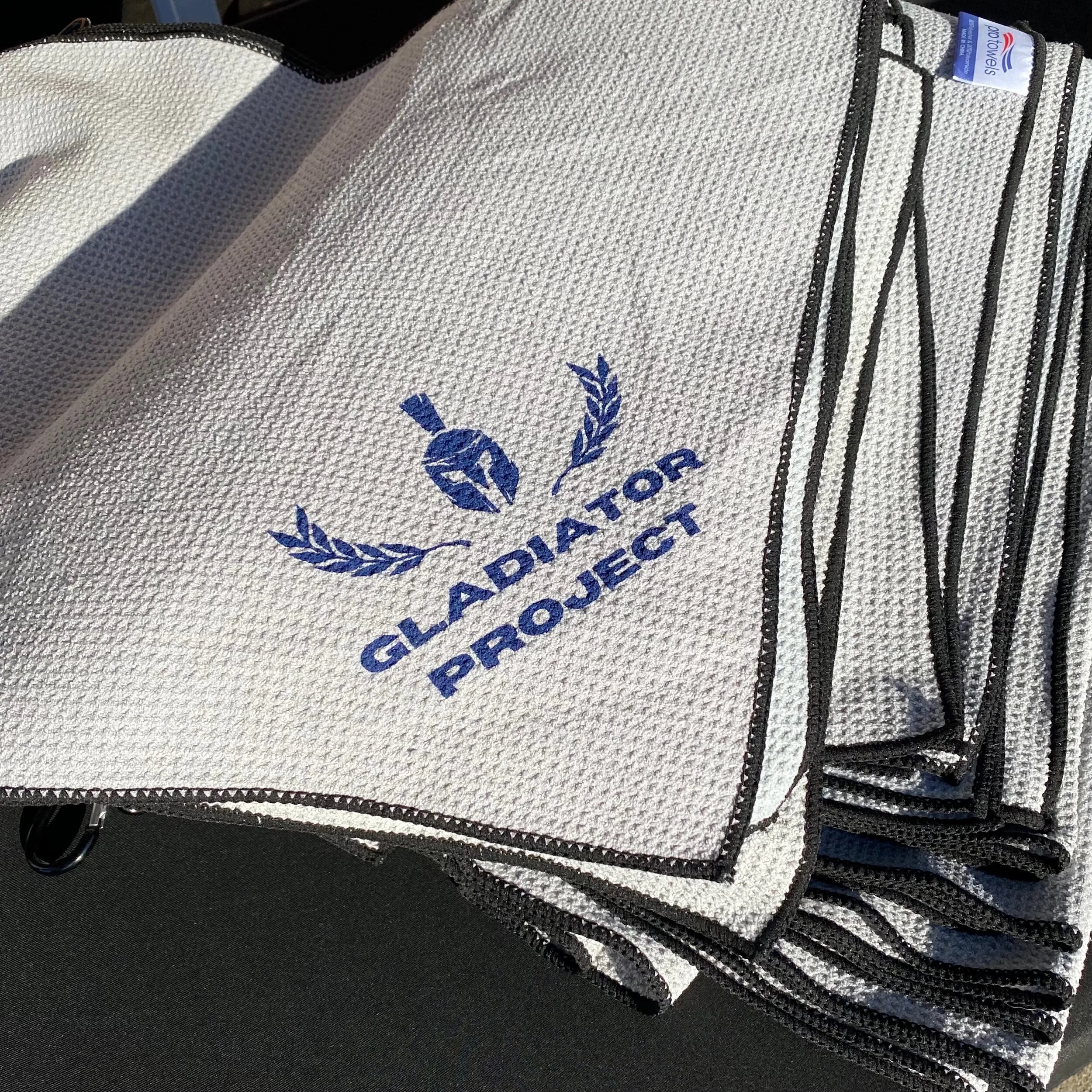 Gray golf towel with blue Gladiator Project logo on corner