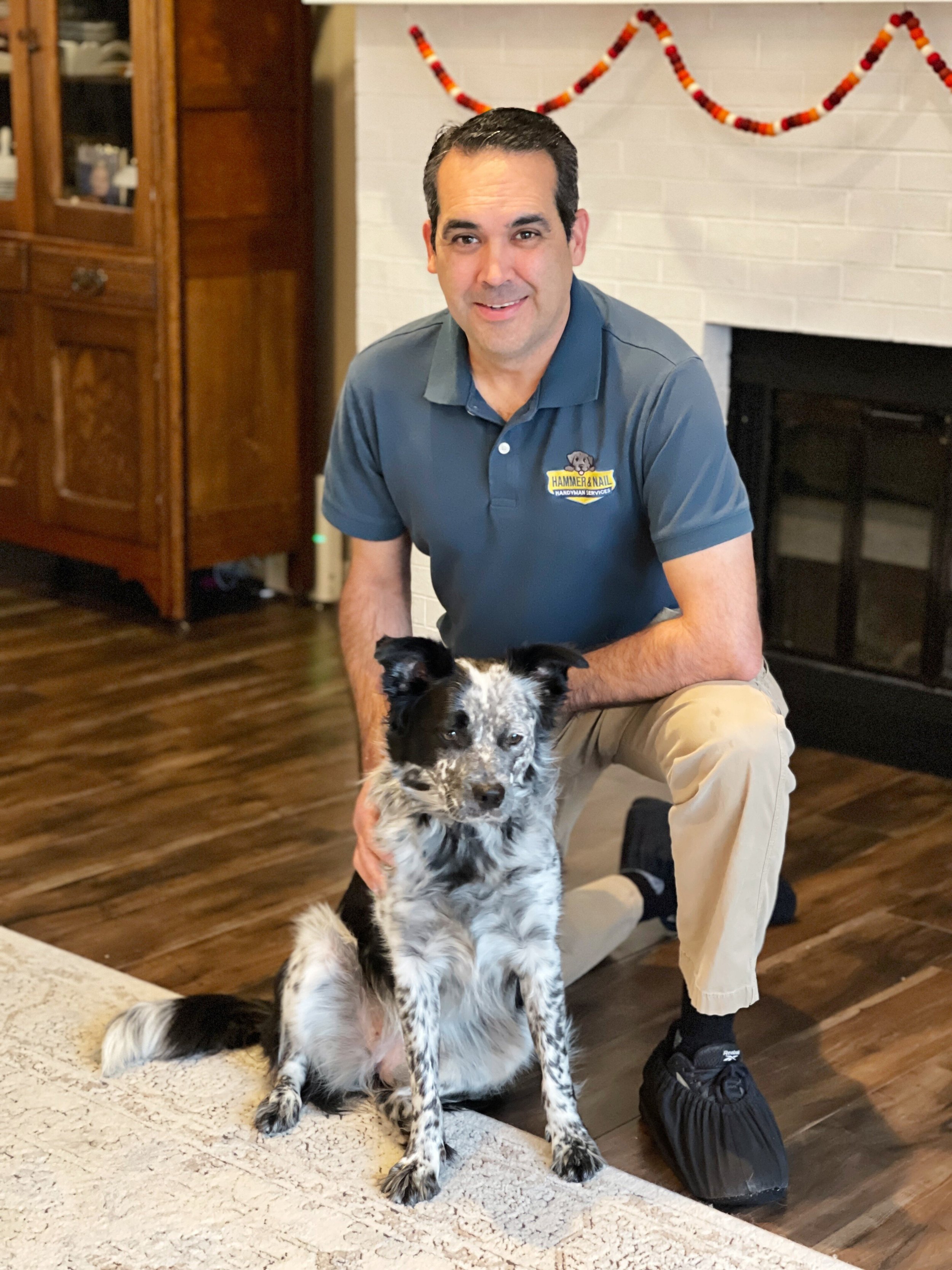 Hammer & Nail Handyman Services employee posing with blue heeler dog in front of fireplace