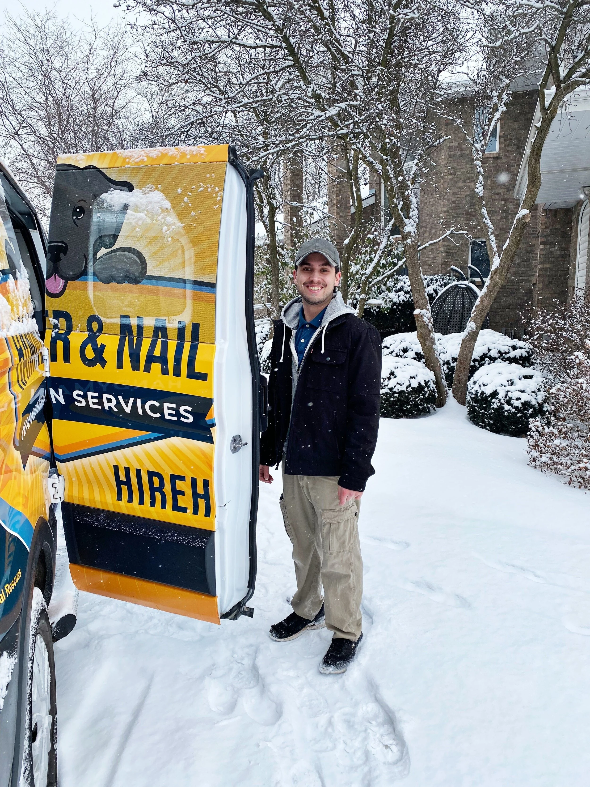 Smiling Hammer & Nail Handyman Services male employee standing next to an open wrapped van door in the snow