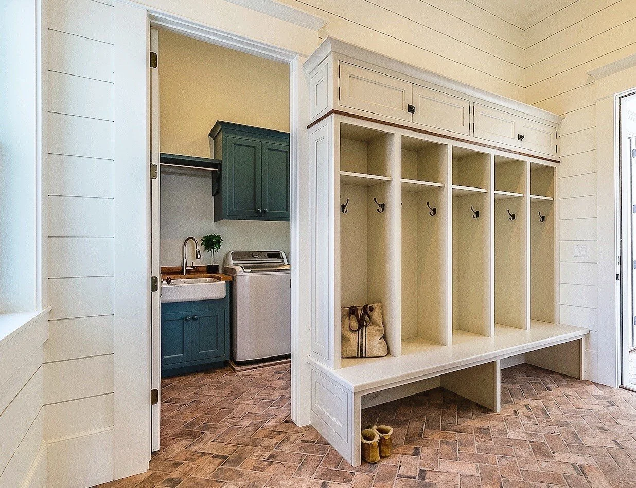 Mudroom with built-in seating and hooks, adjacent to a laundry area with teal cabinets, laundry sink, and washer.