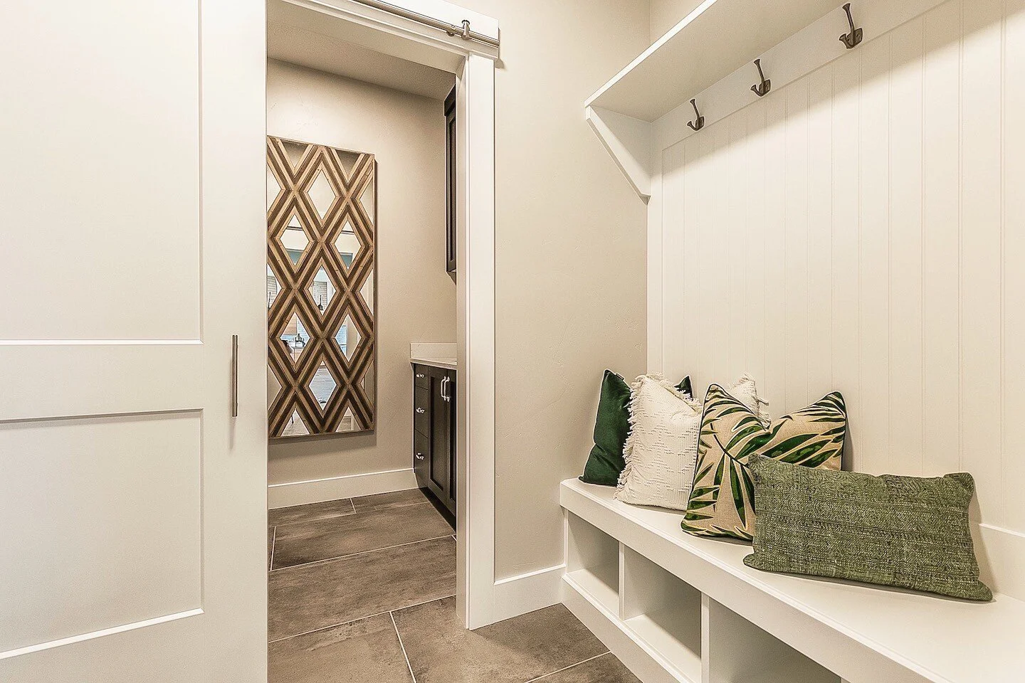 Entryway with a white bench, decorative pillows, hooks for hanging items, and a nursery or child's room visible through a door.