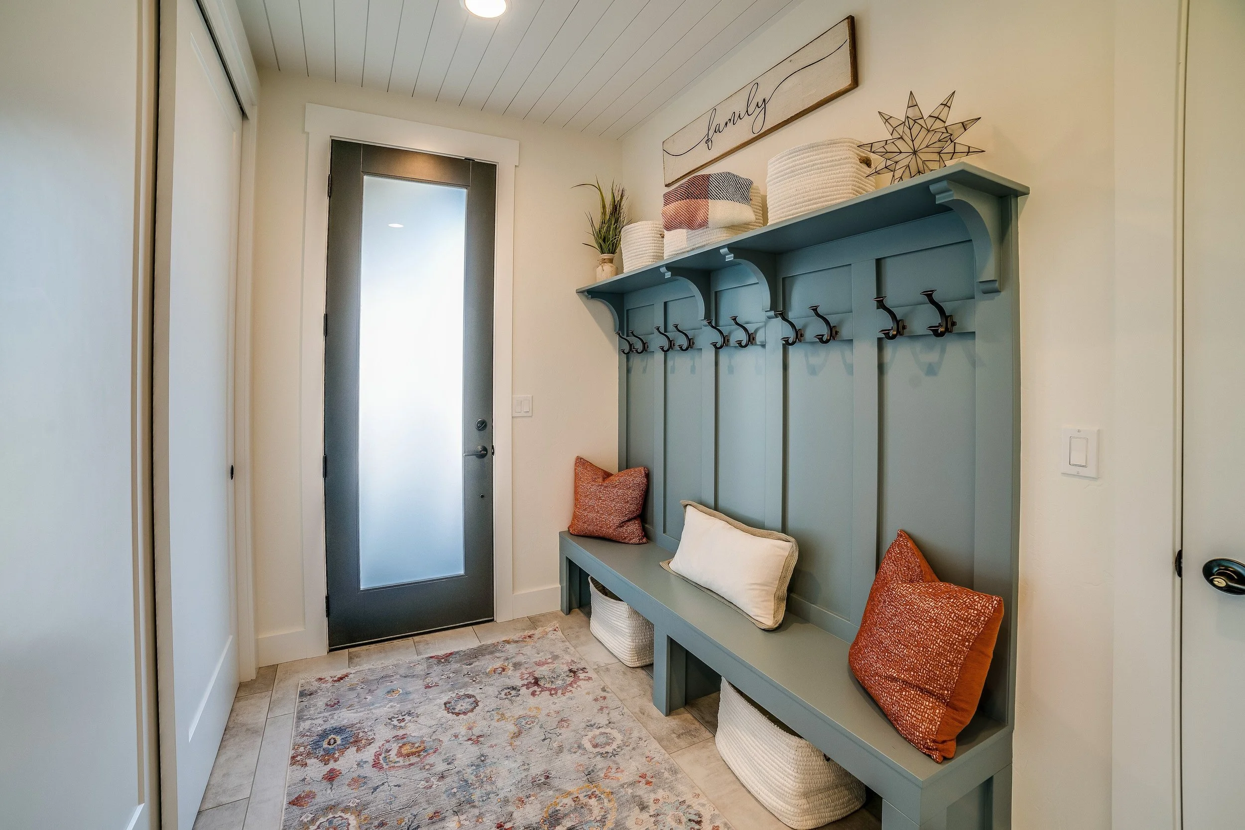 Entryway with a blue built-in bench and coat hooks, decorative pillows, baskets underneath, and a sign that says 'family' above.