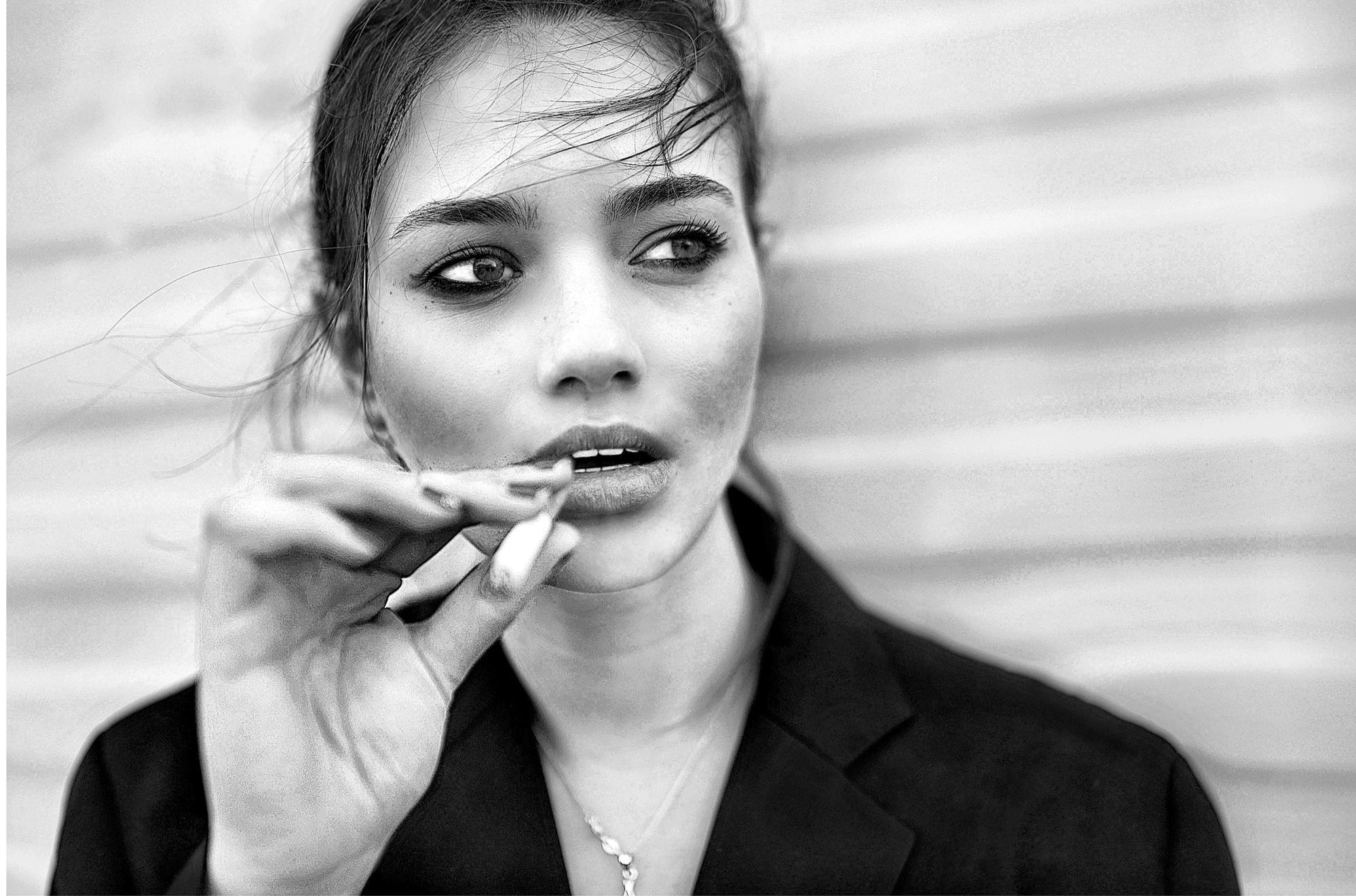 A close-up black and white photo of a young woman with wet hair, holding a cigarette near her lips, looking to the side. She is wearing a dark top and a necklace.