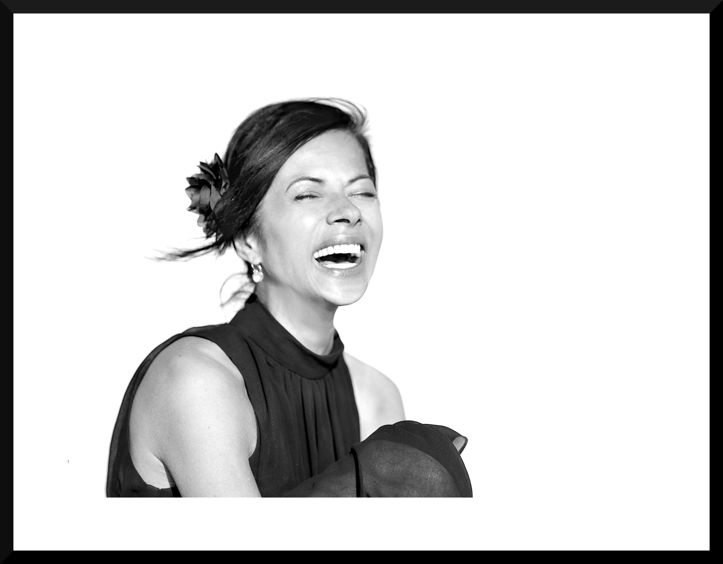 Black and white photograph of a woman with short hair, smiling and wearing earrings, dressed in a sleeveless top, against a plain background.