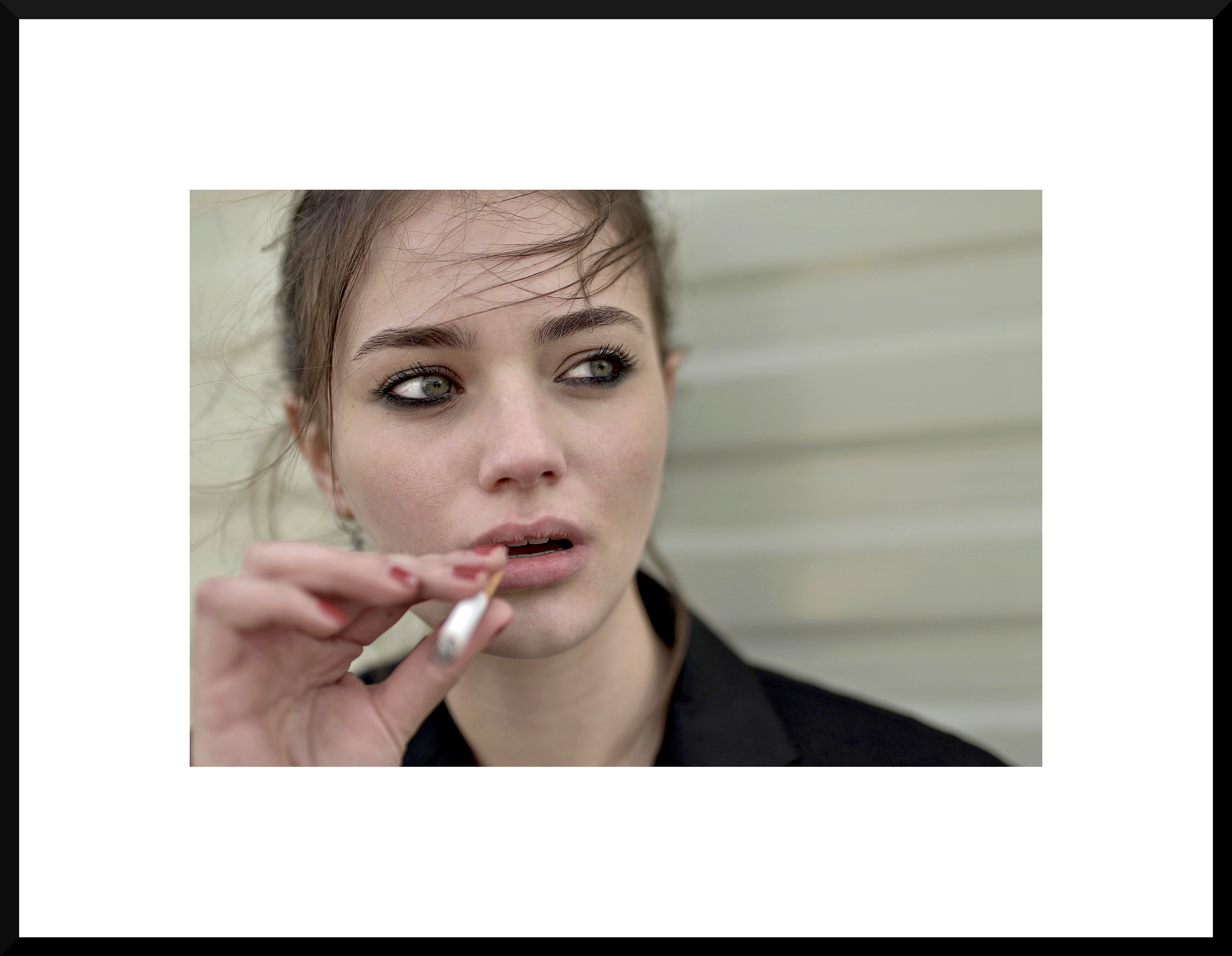 Close-up of a young woman with messy hair and smoky eye makeup smoking a cigarette.