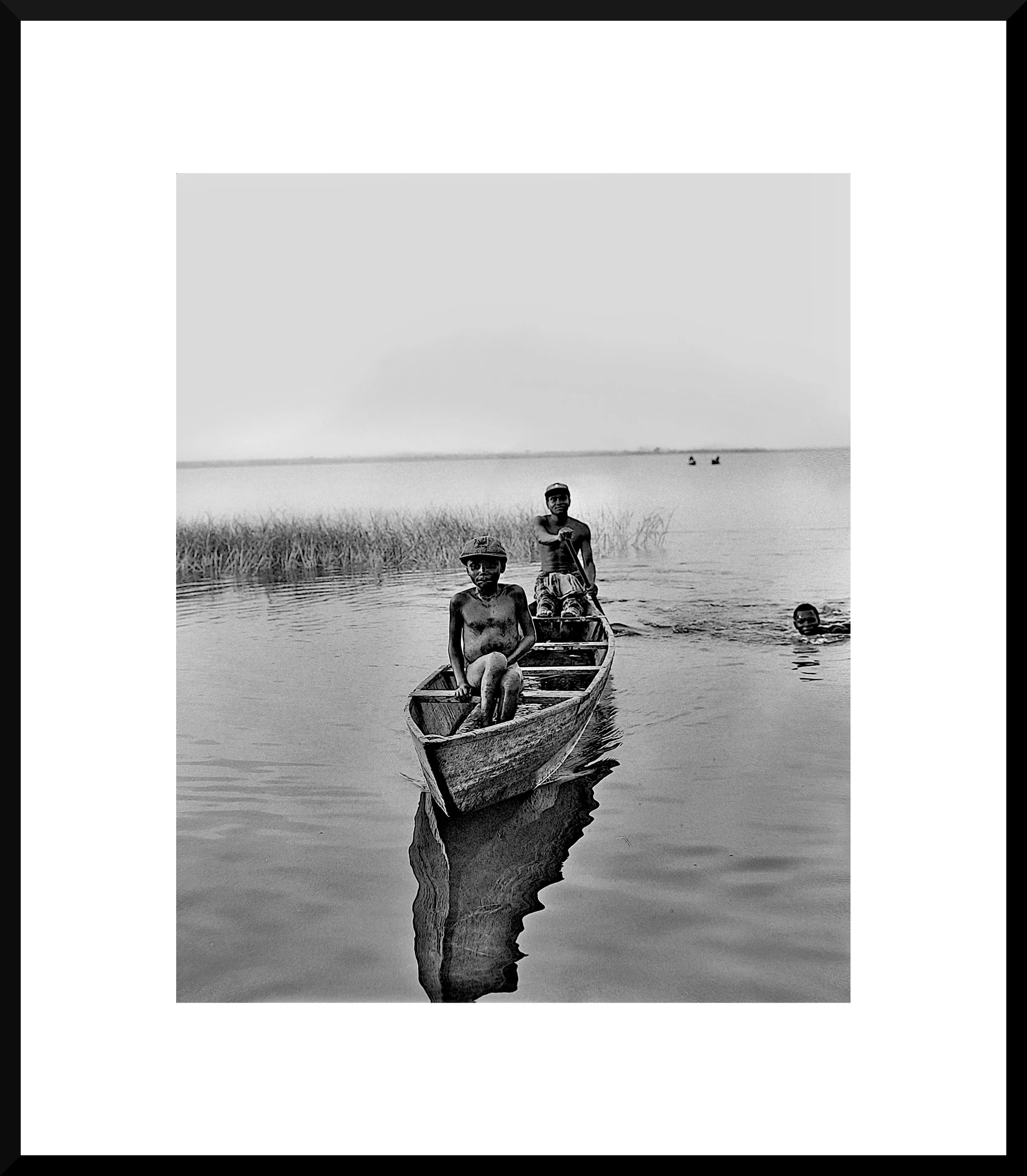 Three people in a small boat on a calm body of water, with one person sitting in the boat and two others standing or swimming nearby.