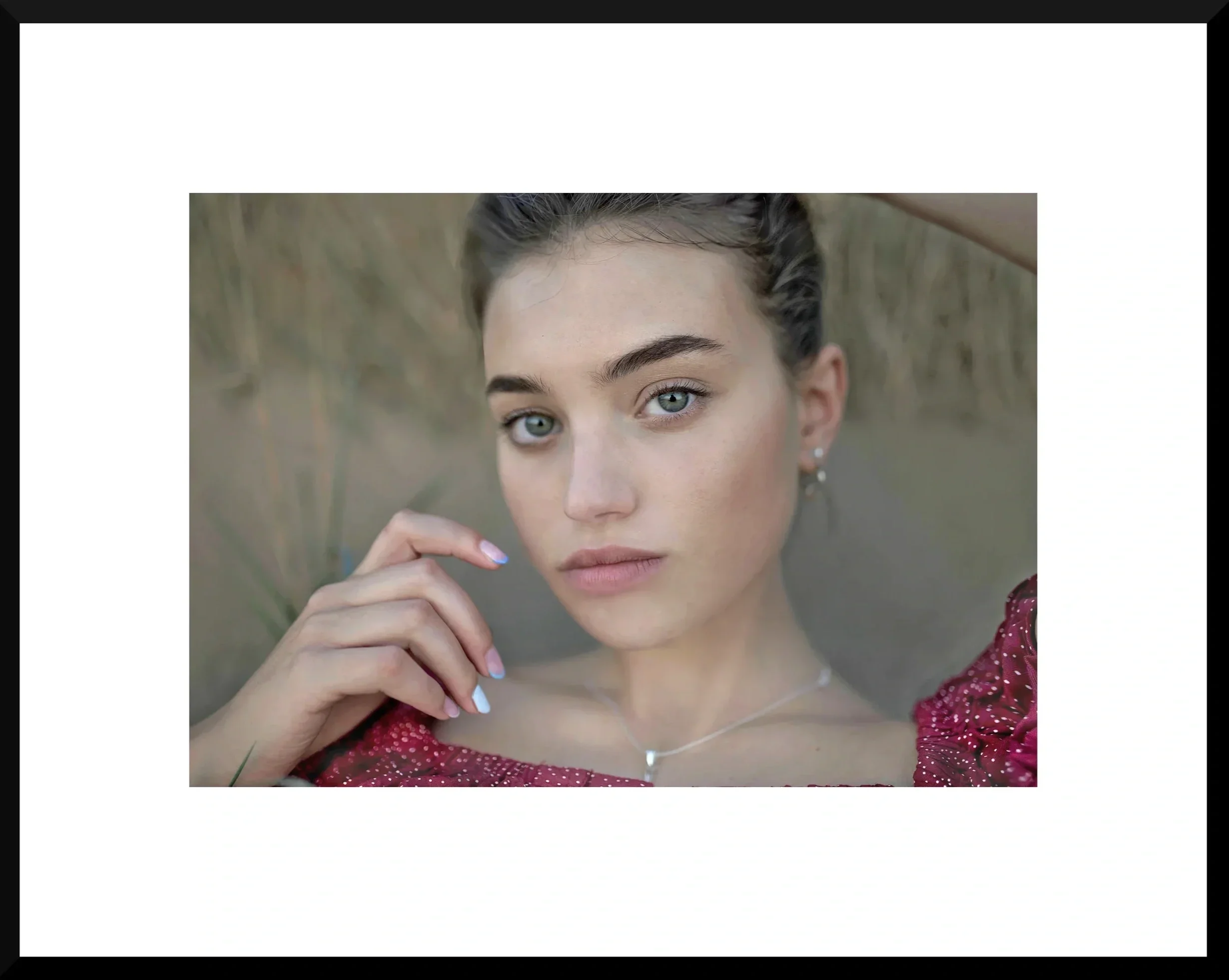 Close-up of a young woman with blue eyes, in a red sparkly top, lying on grass, looking into the camera, with her hand near her face.