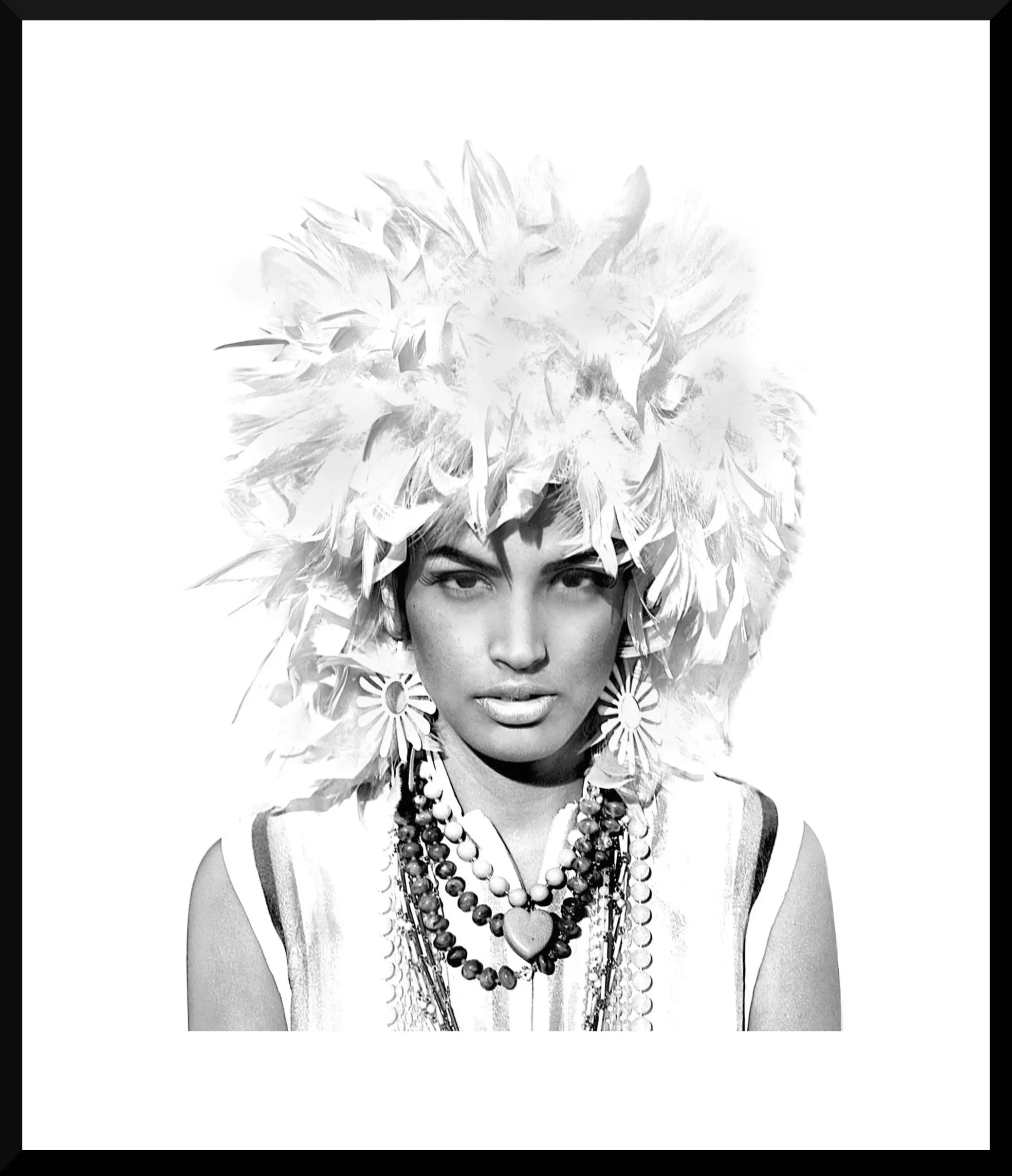 A woman wearing a large feathered headdress, statement earrings, and layered necklaces, photographed in black and white.