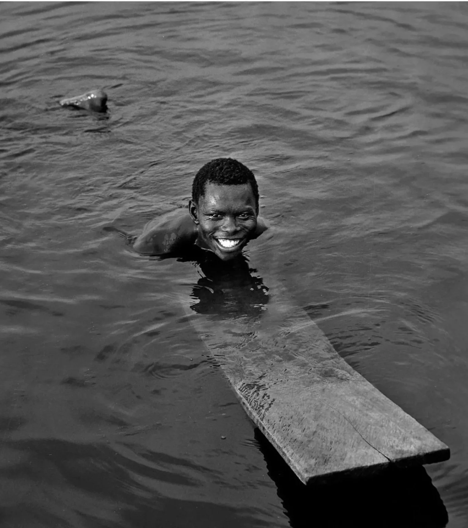 A person smiling in the water near a boat, with the boat's edge visible in the foreground, and water surrounding them.